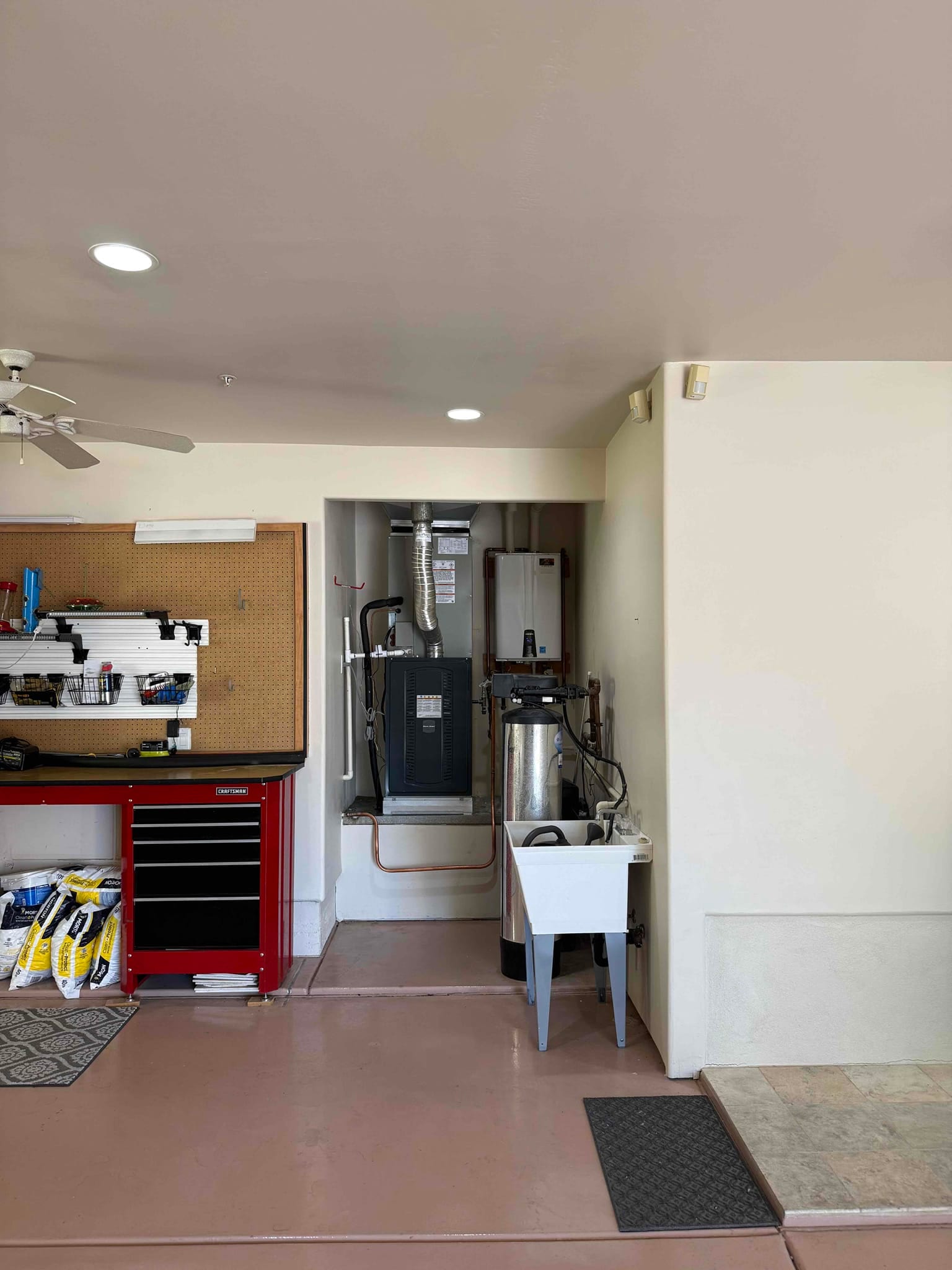 New indoor furnace and coil set on a raised platform with connected duct, copper refrigerant lines, and nearby utility sink in garage alcove.