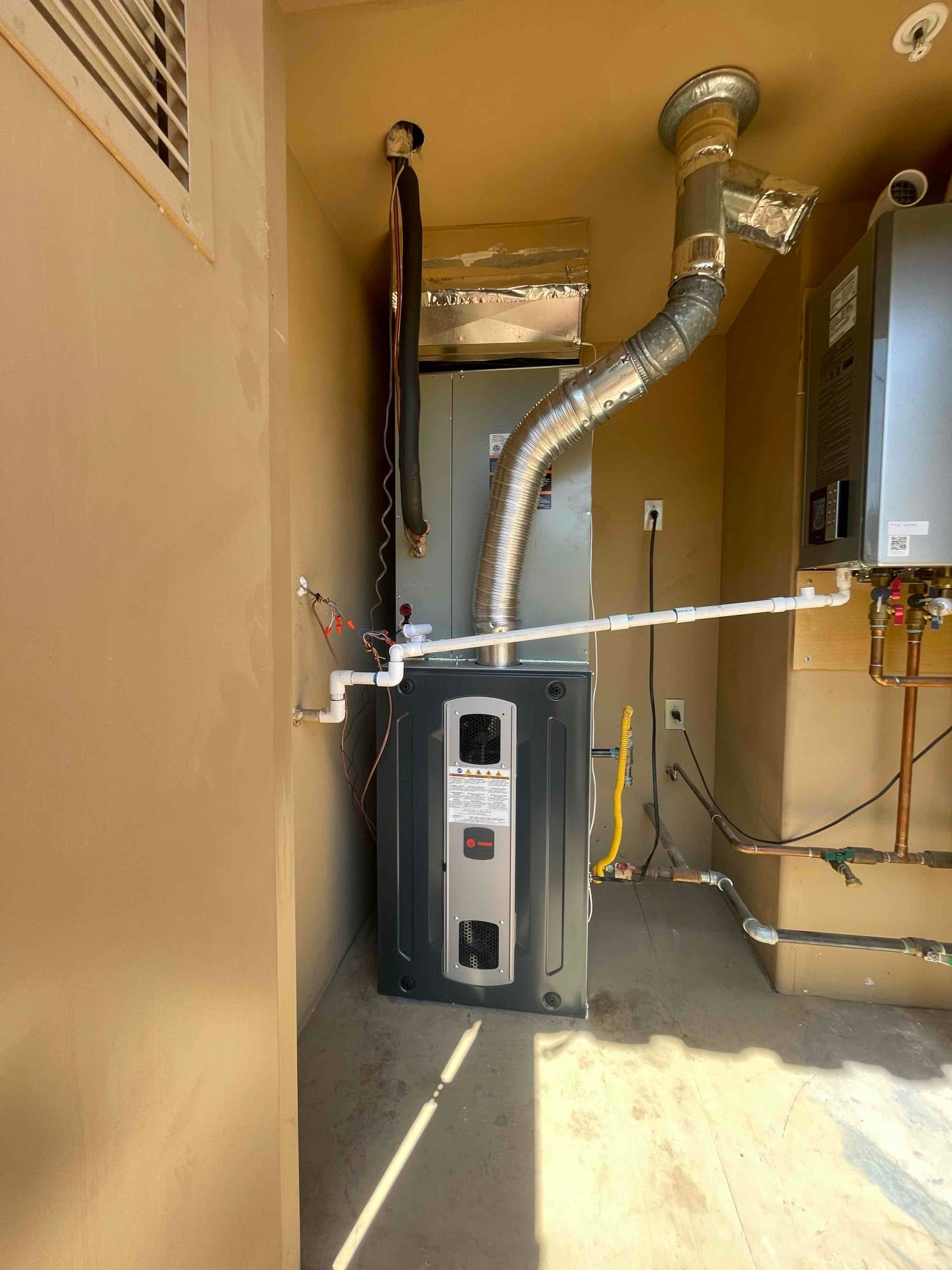 New indoor HVAC equipment installed with sheet metal venting, insulated duct connection, condensate drain, and gas piping in a utility closet.