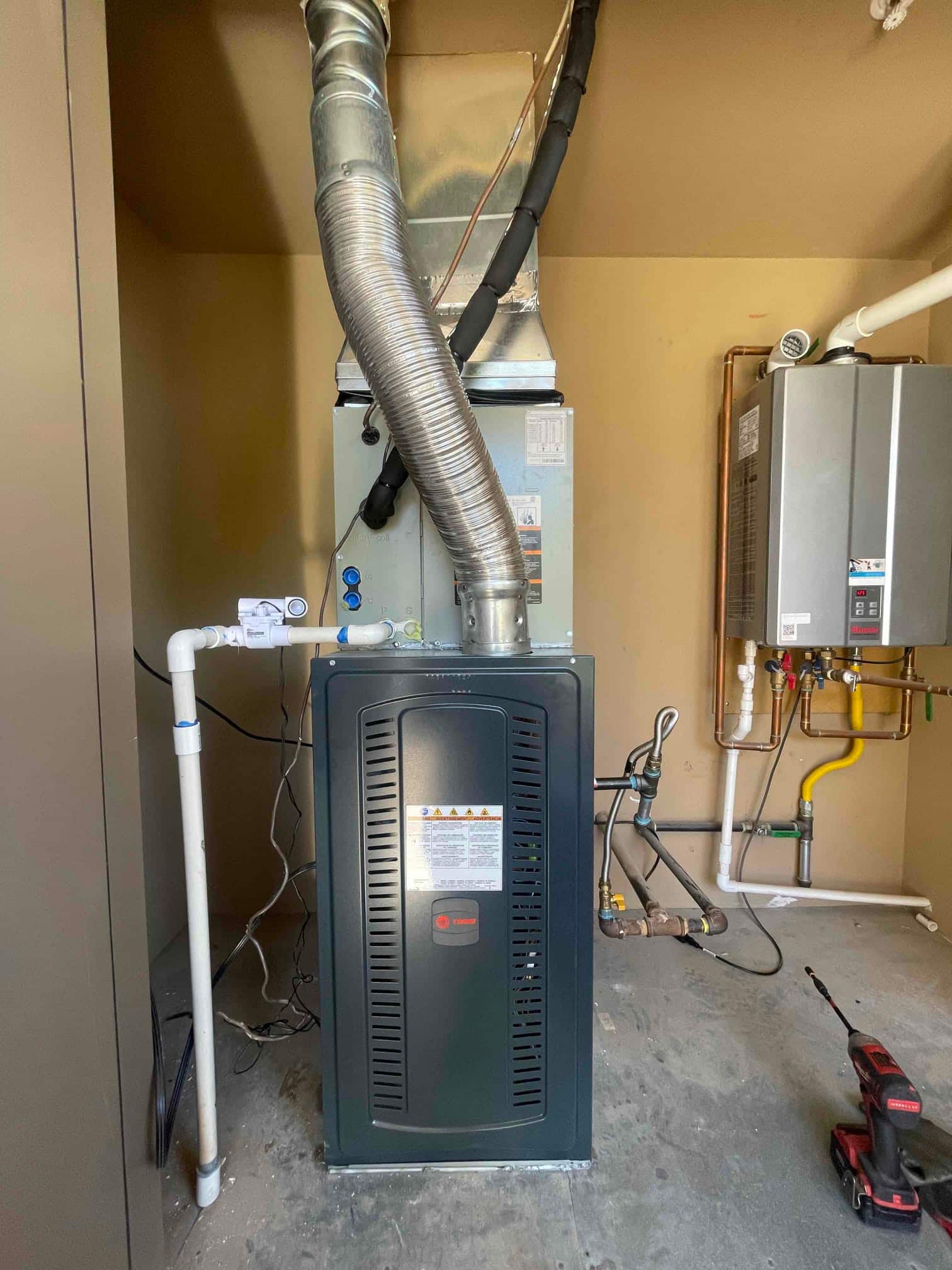 New indoor HVAC installation with furnace, evaporator coil, insulated refrigerant lines, condensate drain, and gas piping neatly routed in the mechanical area.