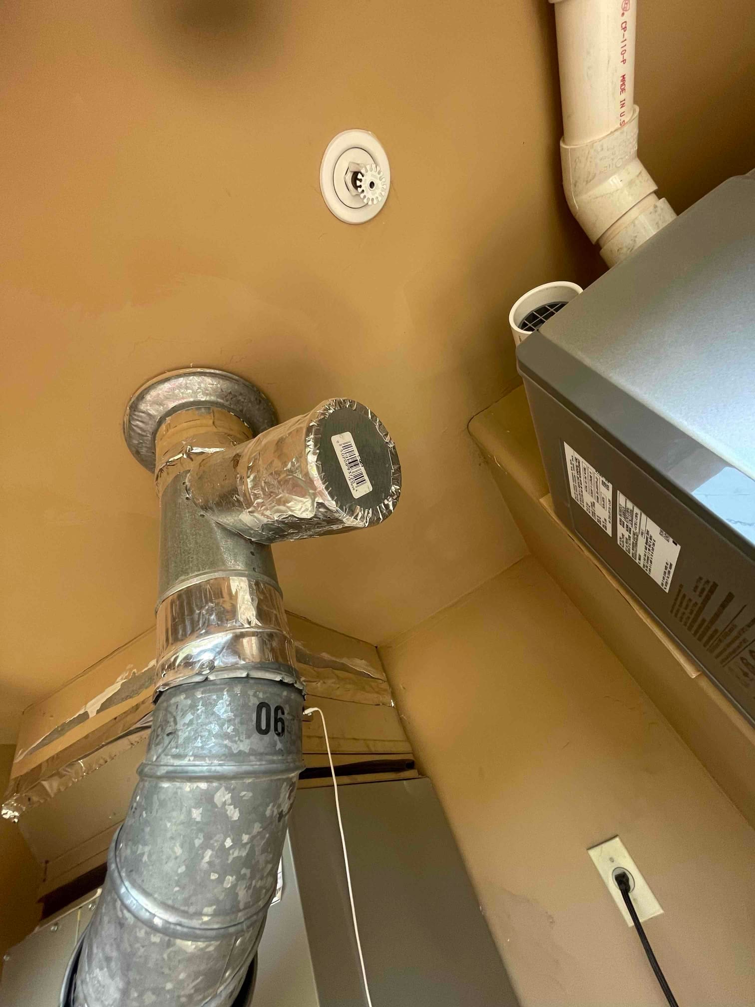 New indoor HVAC installation showing metal flue, sealed duct connections with foil tape, PVC condensate piping, and equipment cabinet in utility area.