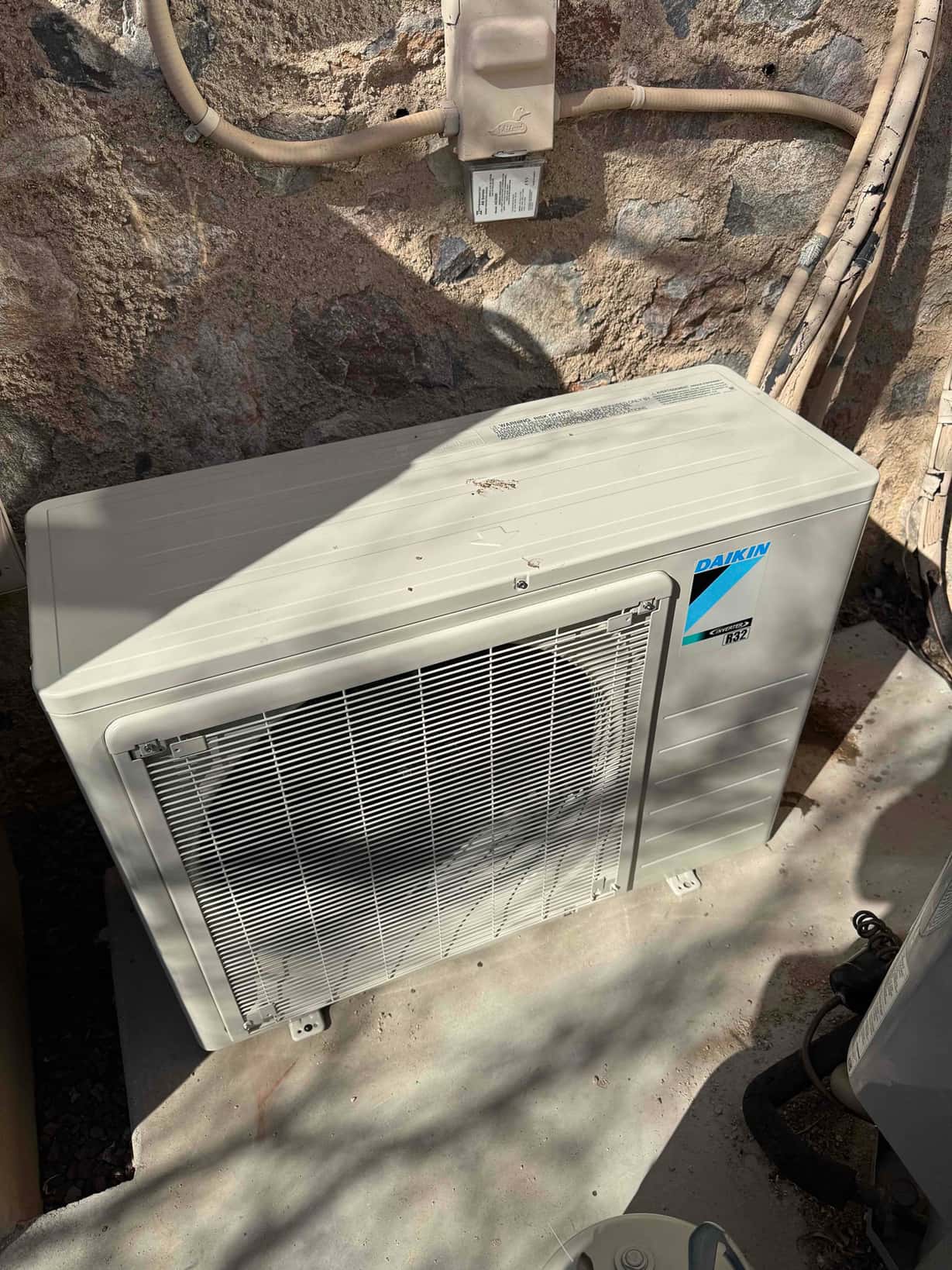 New mini-split outdoor condenser set on a level pad with conduit and disconnect mounted on the wall behind.