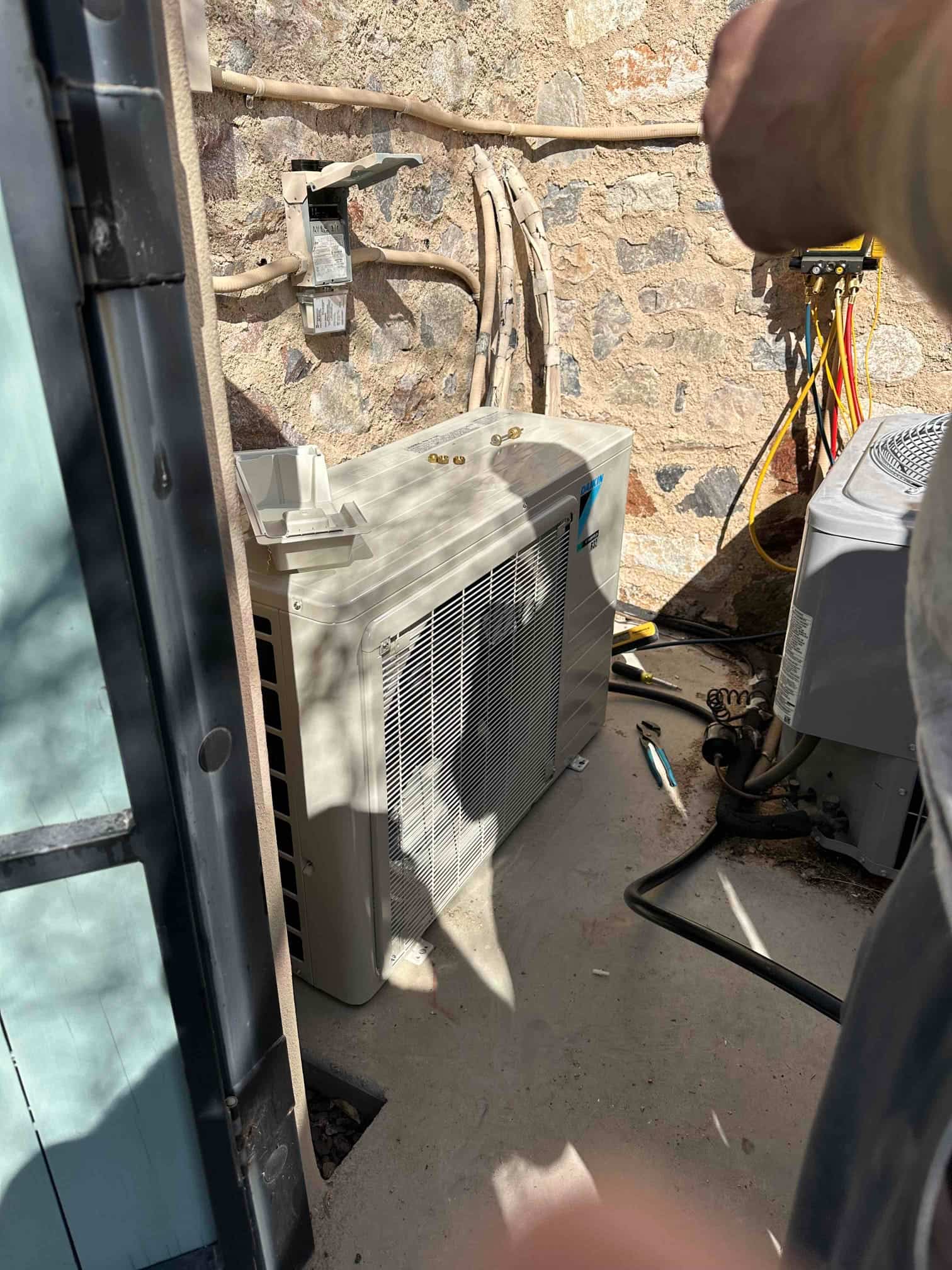 New mini-split outdoor unit set on pad with insulated line sets routed along the wall and disconnect installed nearby.