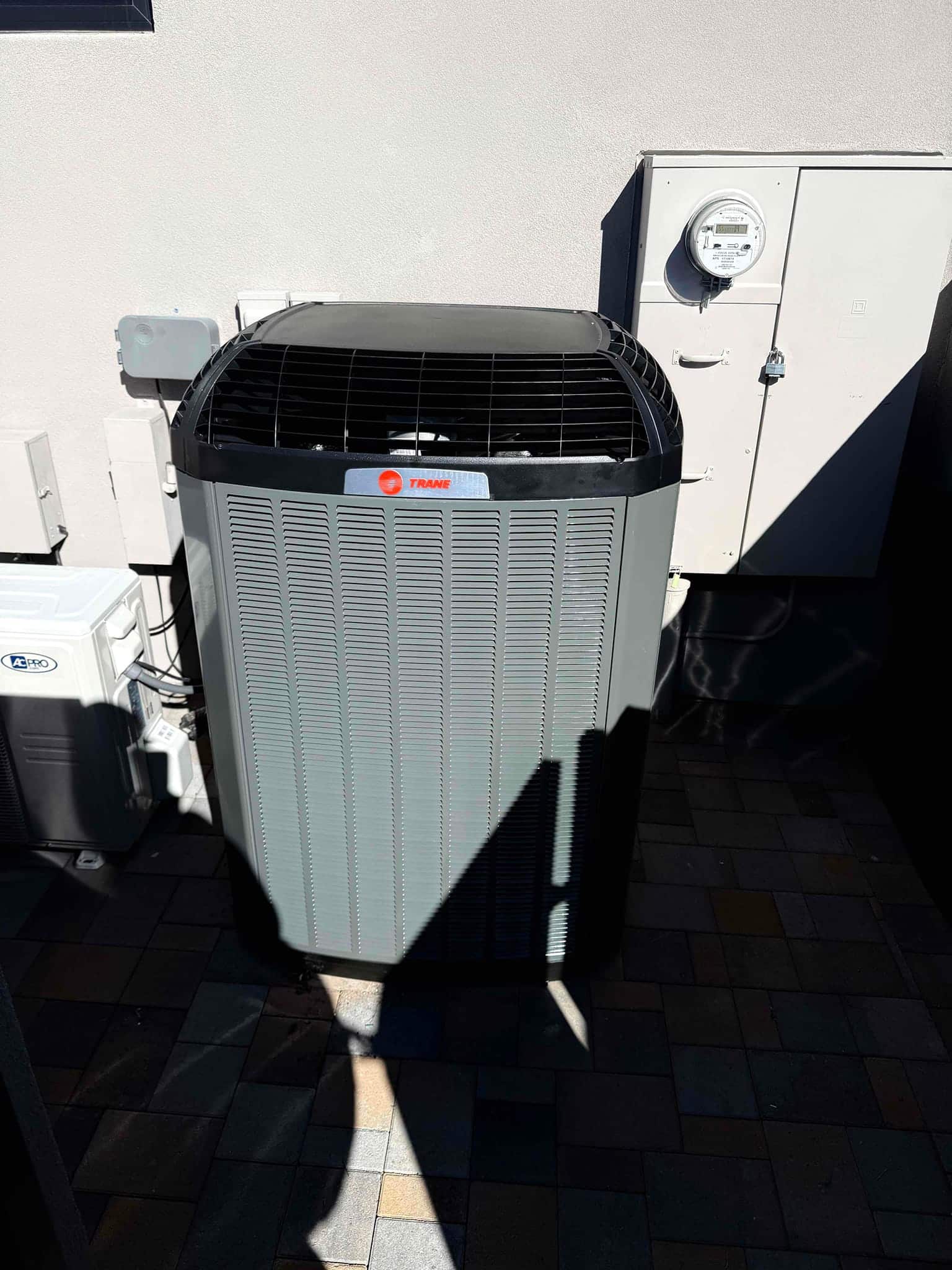 New outdoor condenser installed on a paver pad beside the service disconnect and utility meter with clear airflow around the unit.