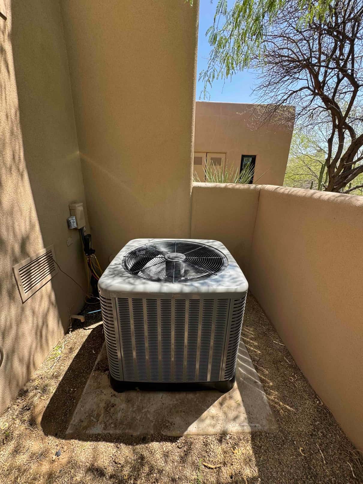 New outdoor condenser set on a concrete pad within a walled alcove, with electrical disconnect and refrigerant line set nearby.