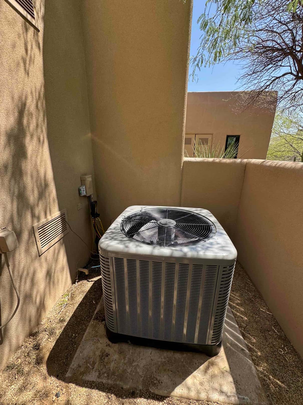 New outdoor condenser set on a concrete pad within a walled alcove, with insulated line set and electrical disconnect nearby.