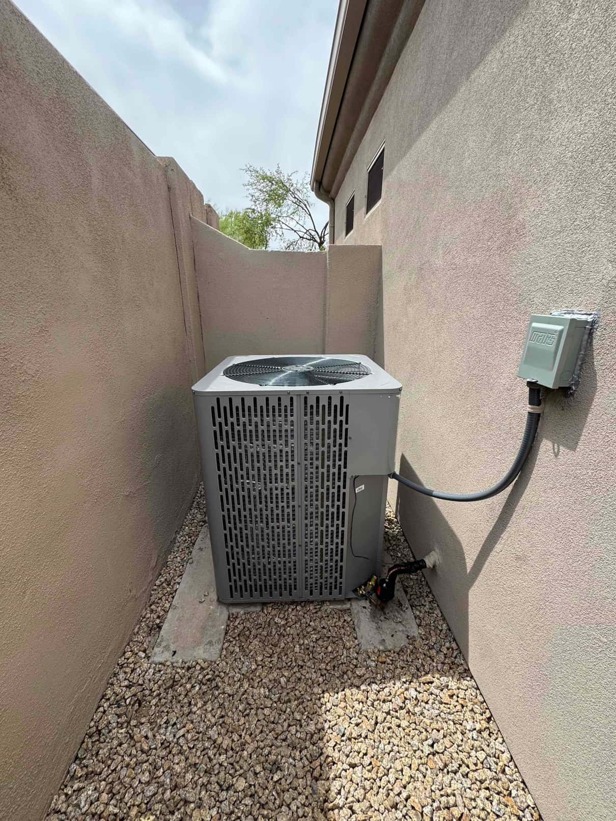 New outdoor condenser set on concrete slabs with insulated refrigerant lines and weatherproof disconnect mounted on the wall.