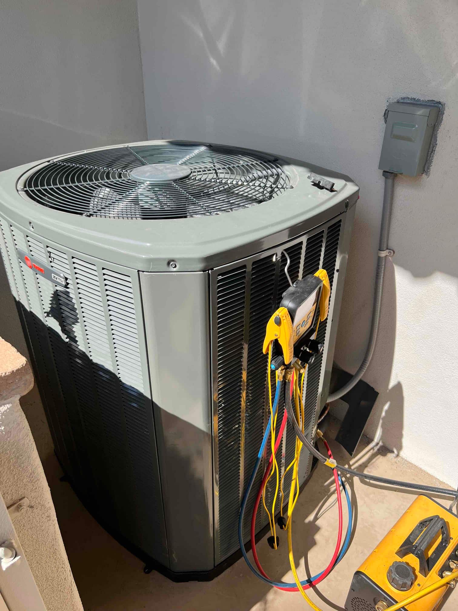 New outdoor condenser set on a level pad with disconnect box and manifold hoses connected during commissioning.