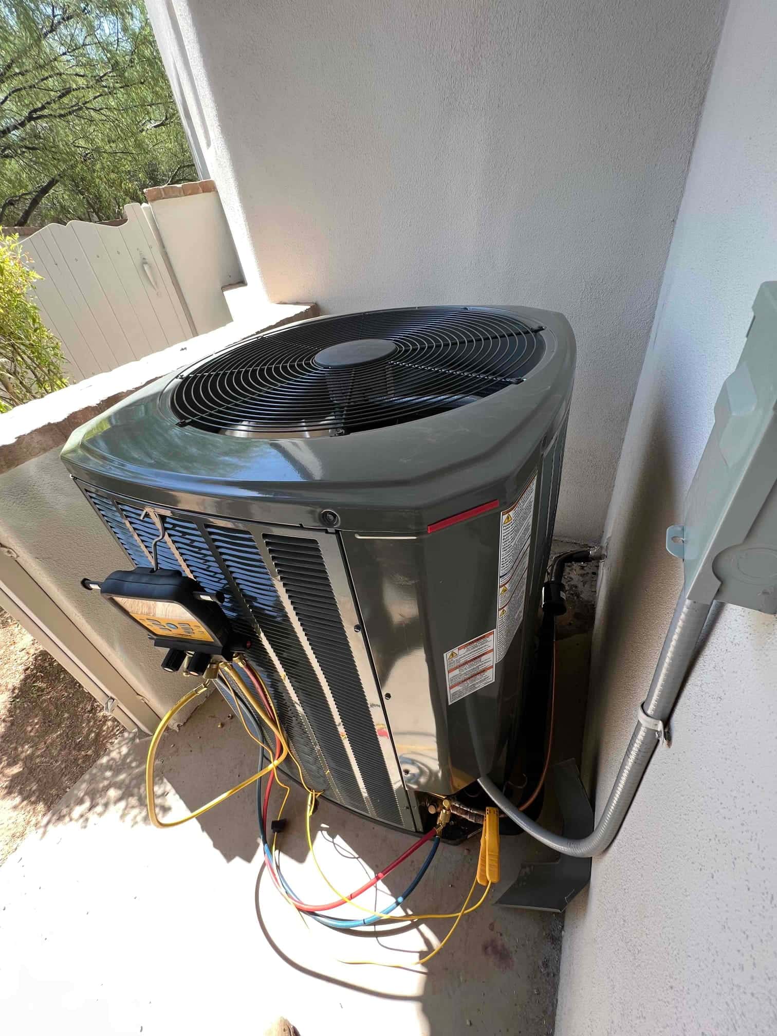New outdoor condenser set on a level pad with disconnect, insulated line set, and manifold hoses connected for commissioning.