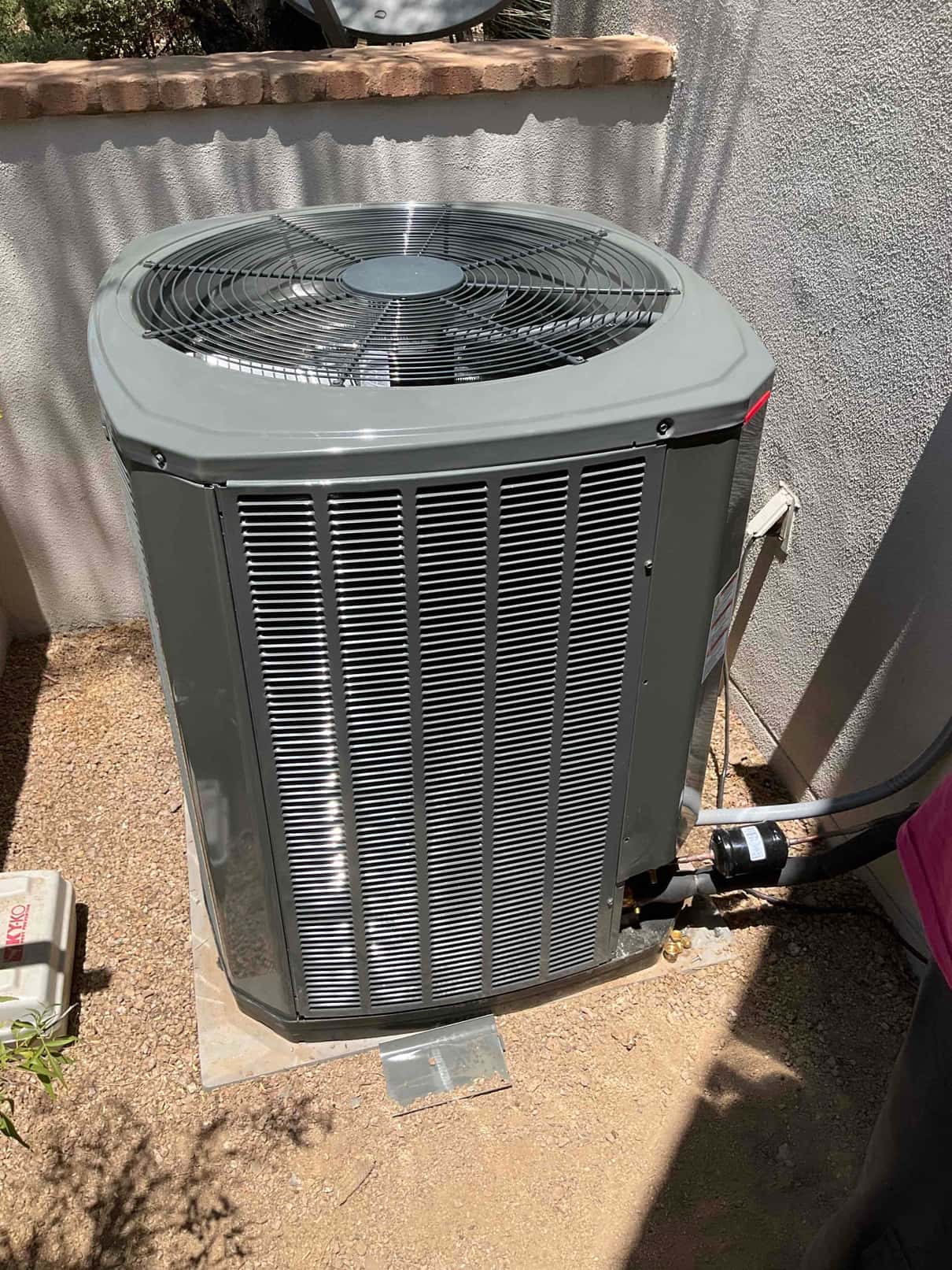New outdoor condenser set on a level pad with insulated refrigerant lines and electrical whip connected at the wall disconnect.