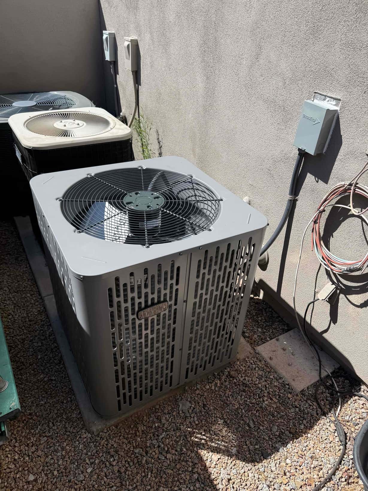New outdoor condenser set on a level pad with whip to the disconnect and adjacent existing units along the wall.