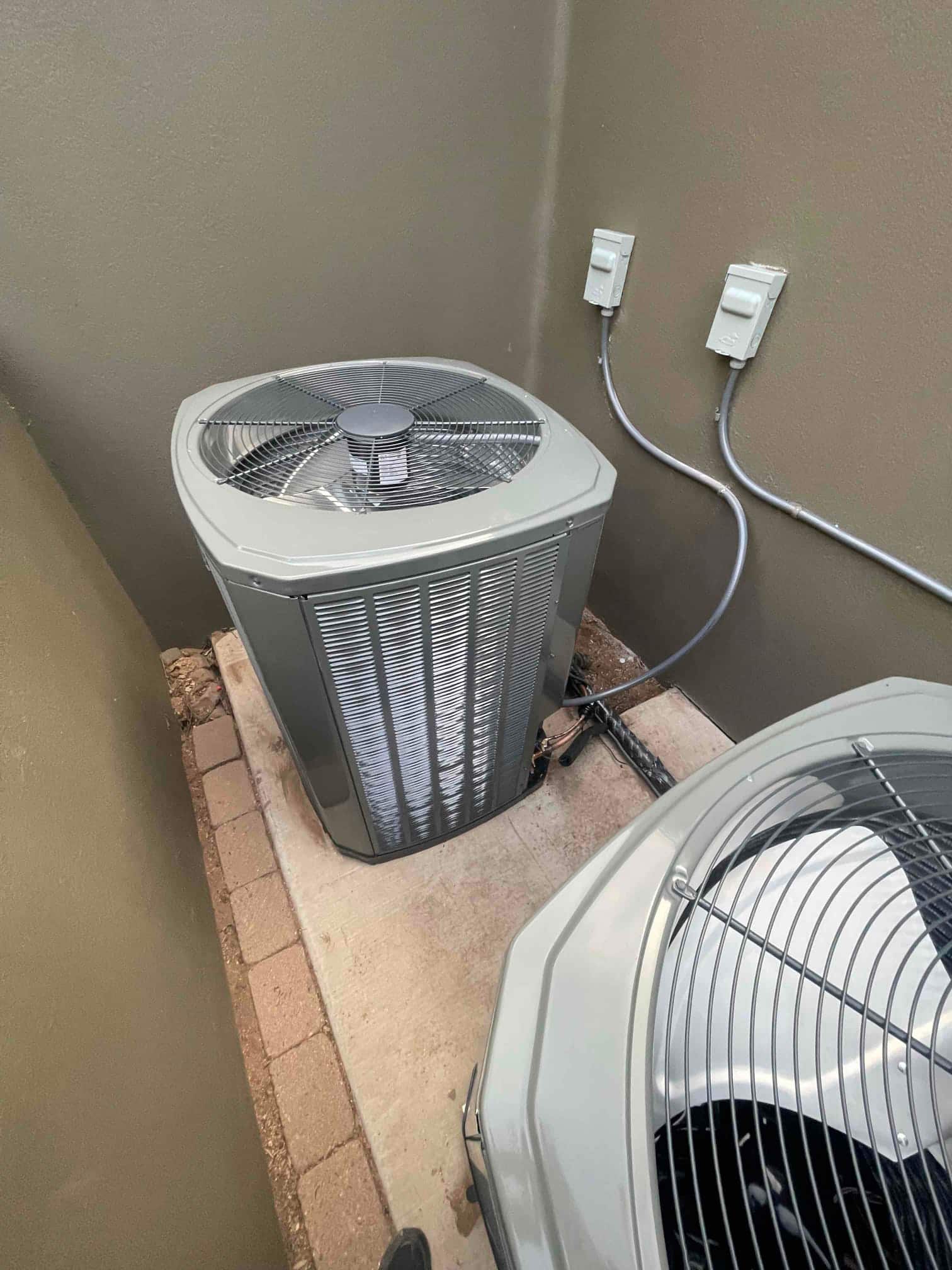 Two new outdoor condensers set on a concrete pad with flexible conduits to dedicated disconnect boxes on the wall.