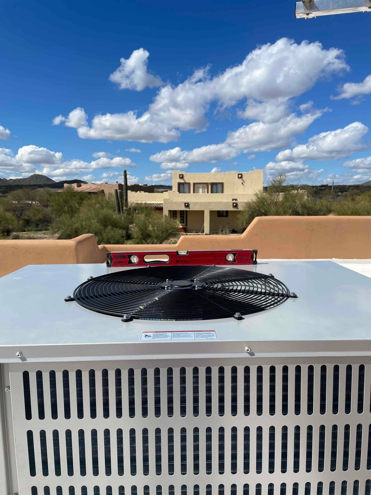 New rooftop condenser set level with a bubble level on top, showing the fan guard and cabinet under clear skies.