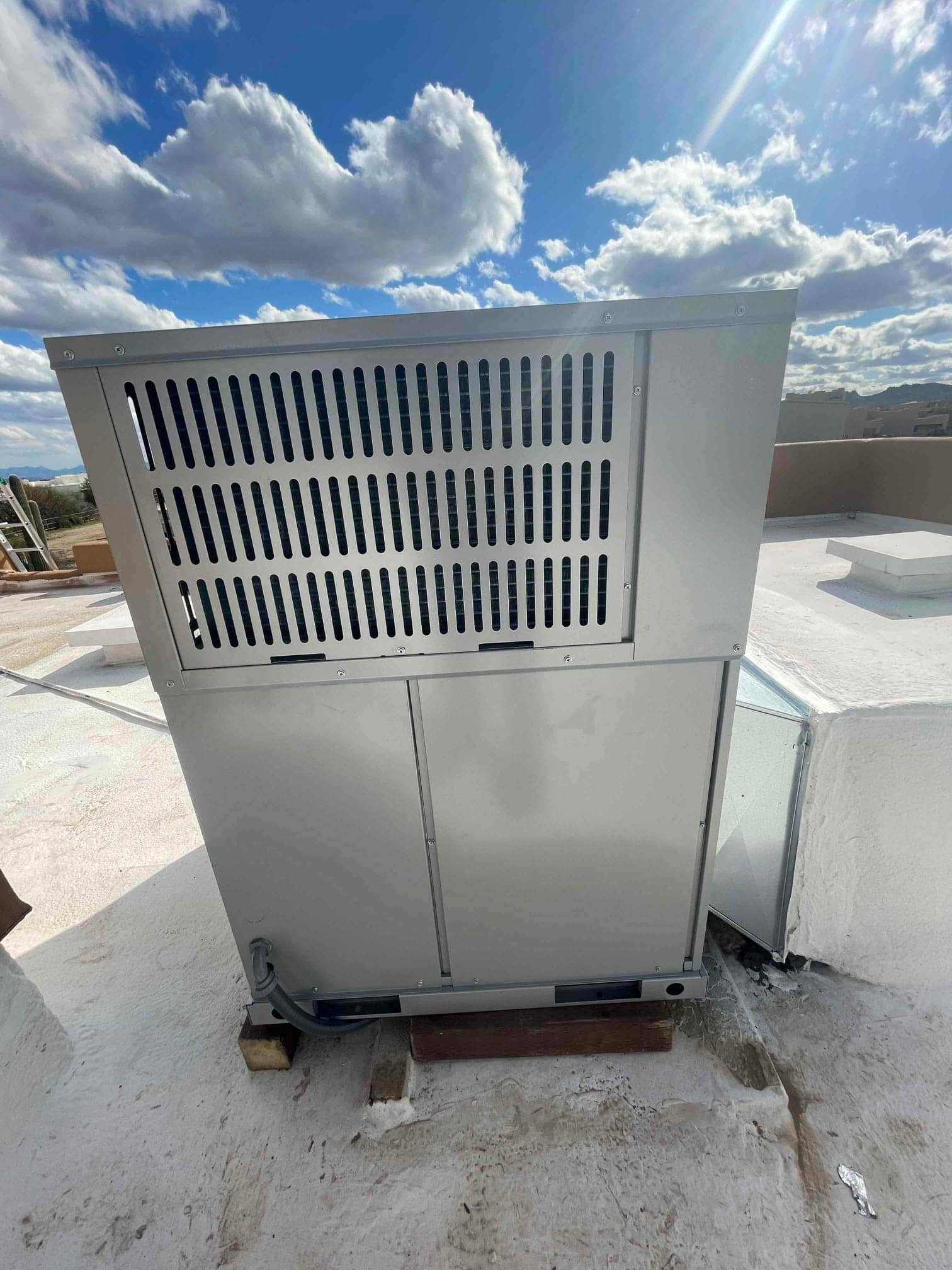 New rooftop HVAC unit set on blocking with sealed curb connection and flexible electrical whip routed to the cabinet.