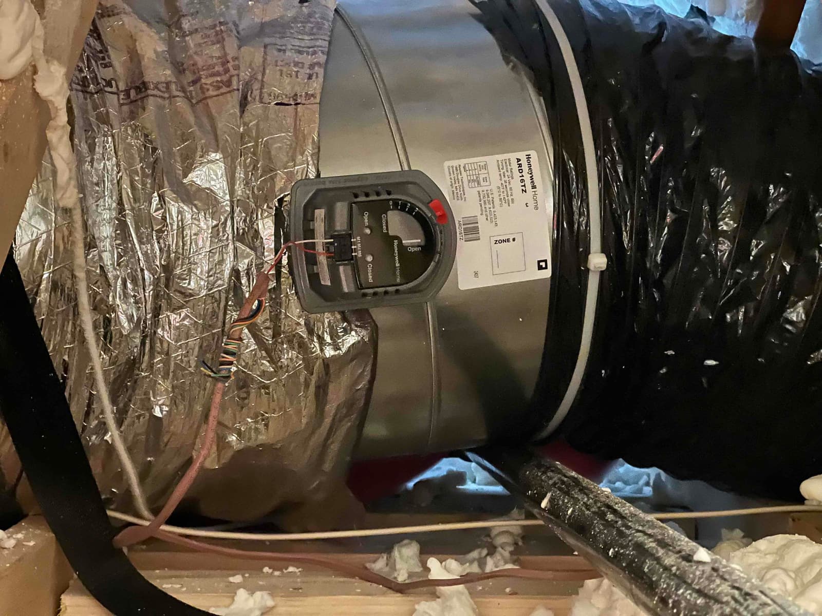 New round zone damper with motor installed in attic ductwork, showing sealed connections and control wiring routed to the actuator.