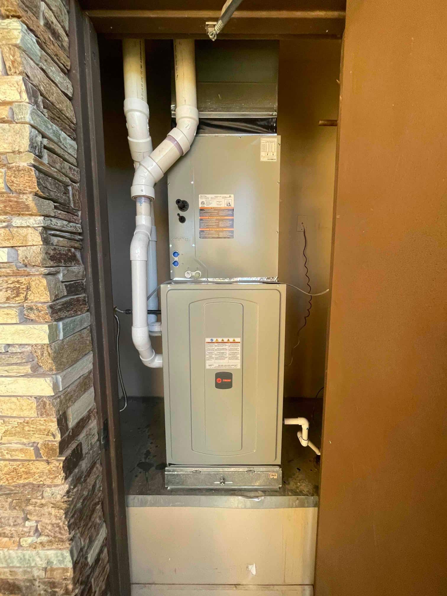New two-stage furnace installed on a platform with PVC venting, condensate drain, and connected ductwork inside the closet alcove.