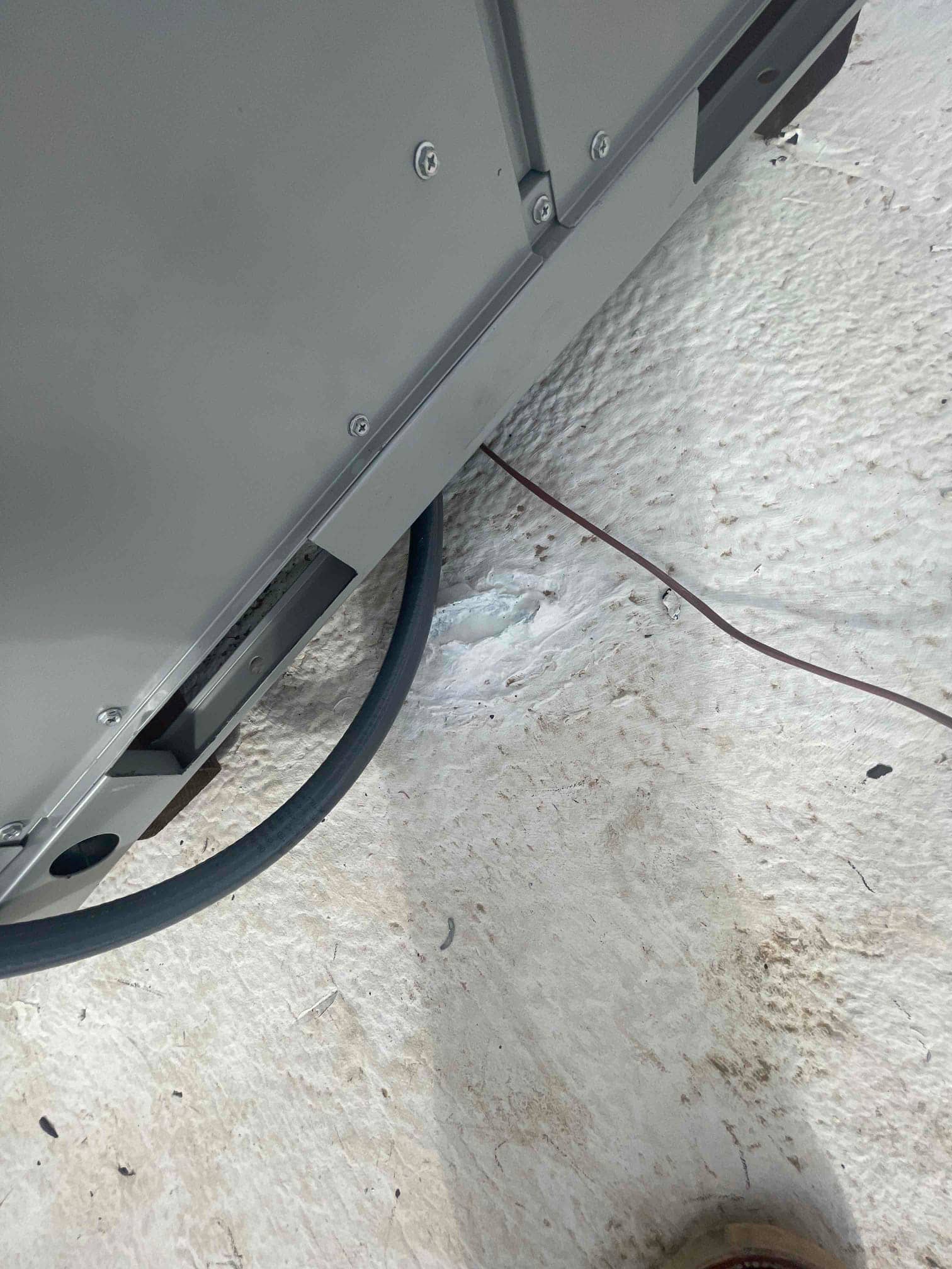 Outdoor condenser base with electrical whip routed into the cabinet and sealed penetration on a concrete pad.