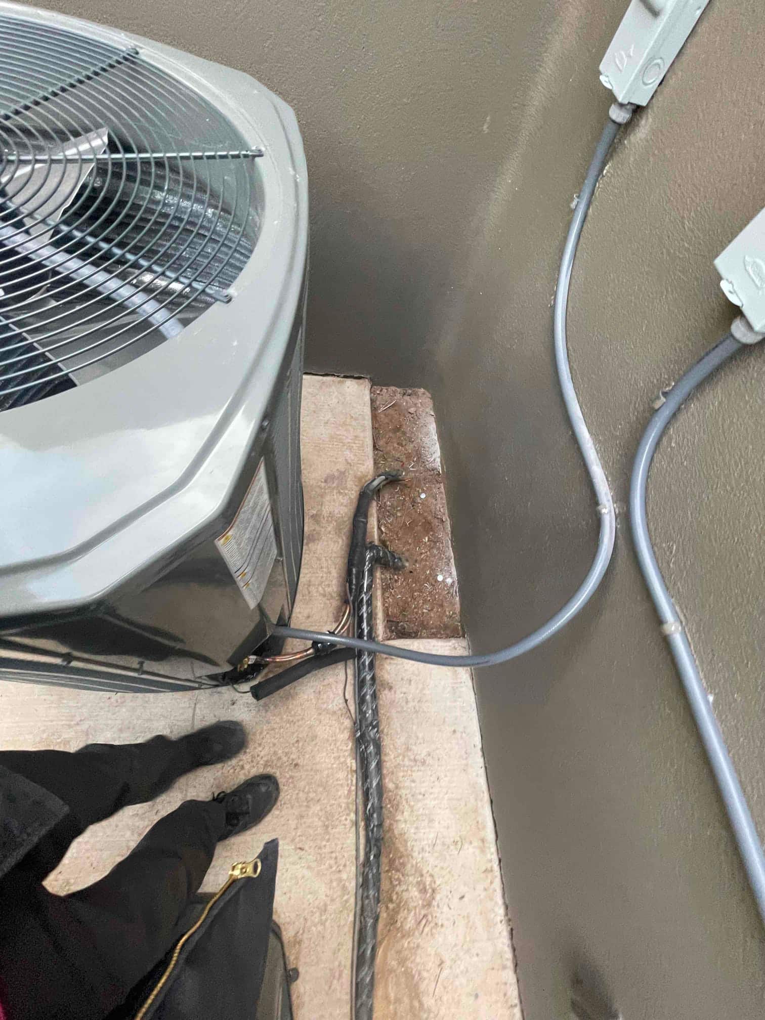 Outdoor condenser set beside wall with new electrical whip, insulated refrigerant line set, and disconnects mounted on the exterior.