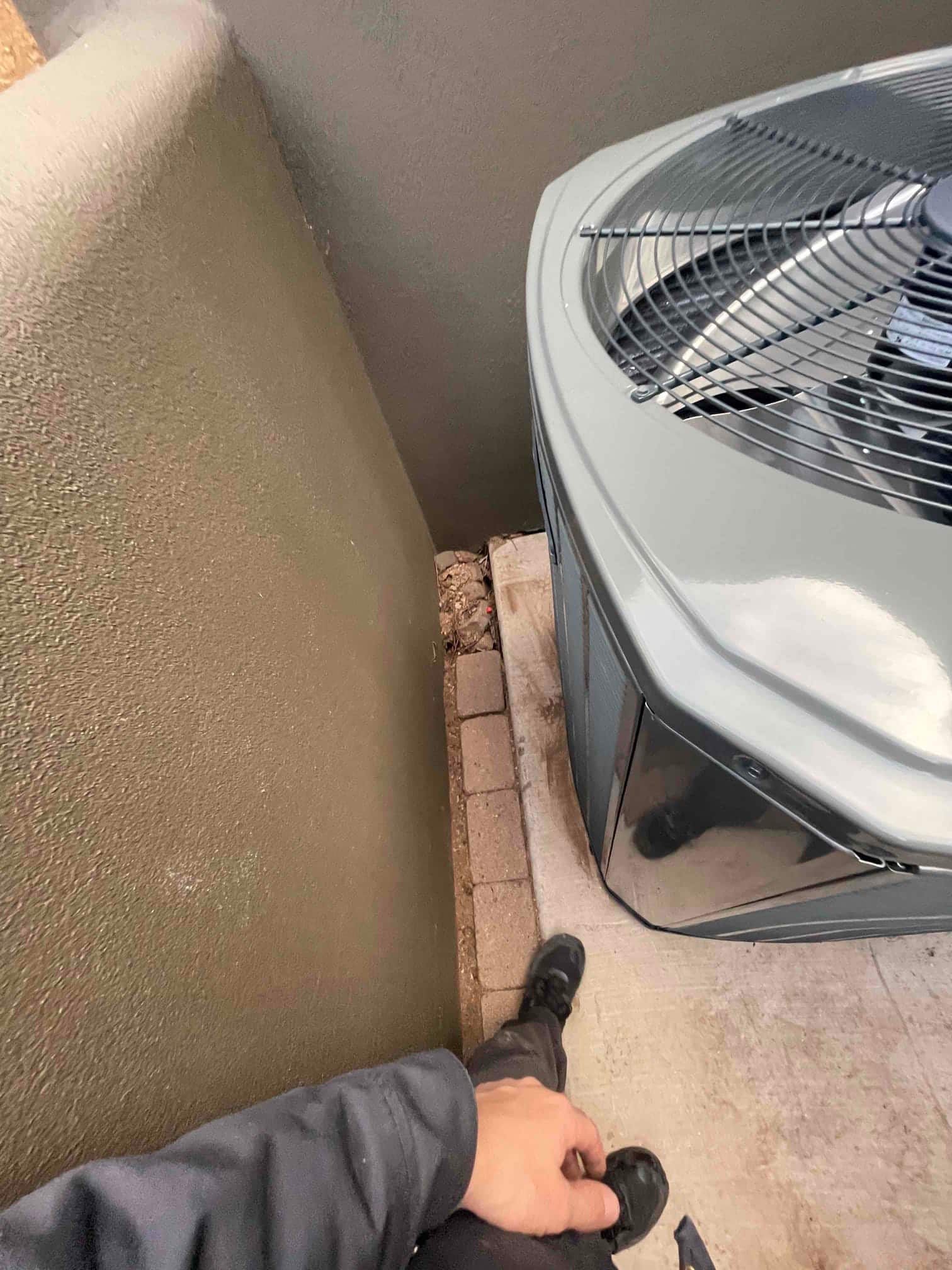 Outdoor condenser set on a concrete pad beside a stucco wall with surrounding paver border visible at the base.