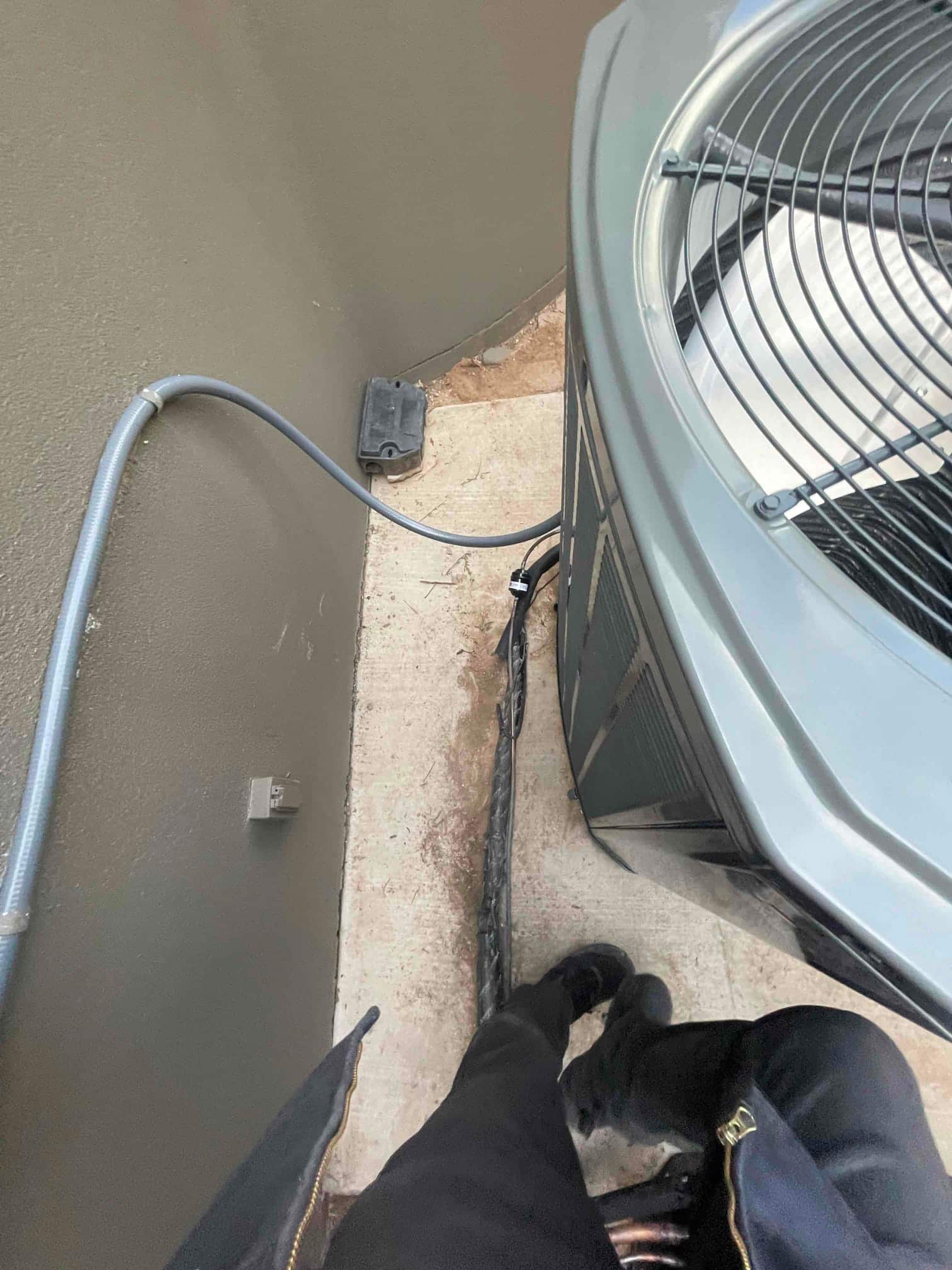 Outdoor condenser set on a concrete pad with flexible electrical conduit and insulated line set routed to the wall disconnect.