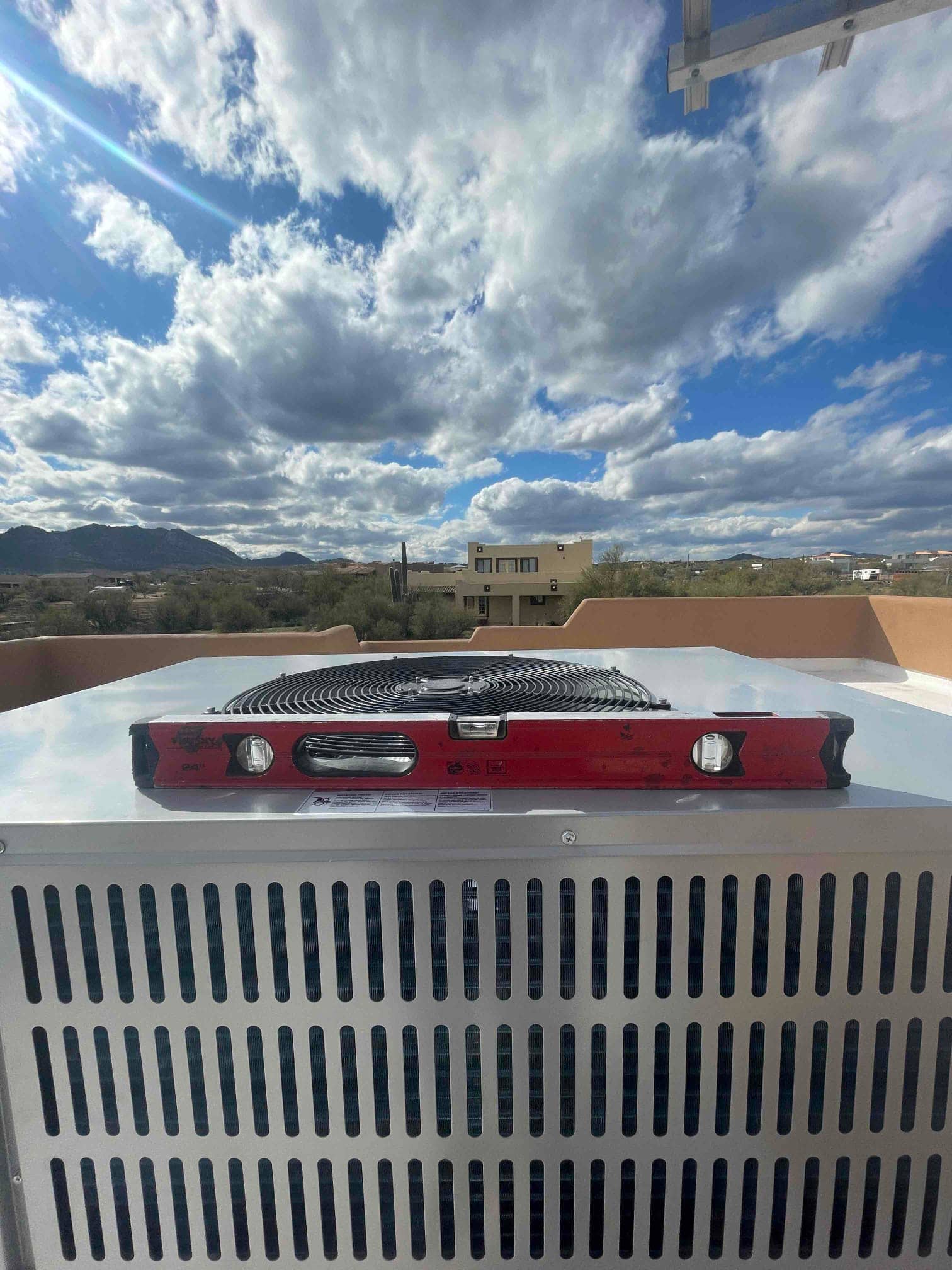Outdoor condenser set level on a rooftop pad, with a bubble level on top to verify proper installation.