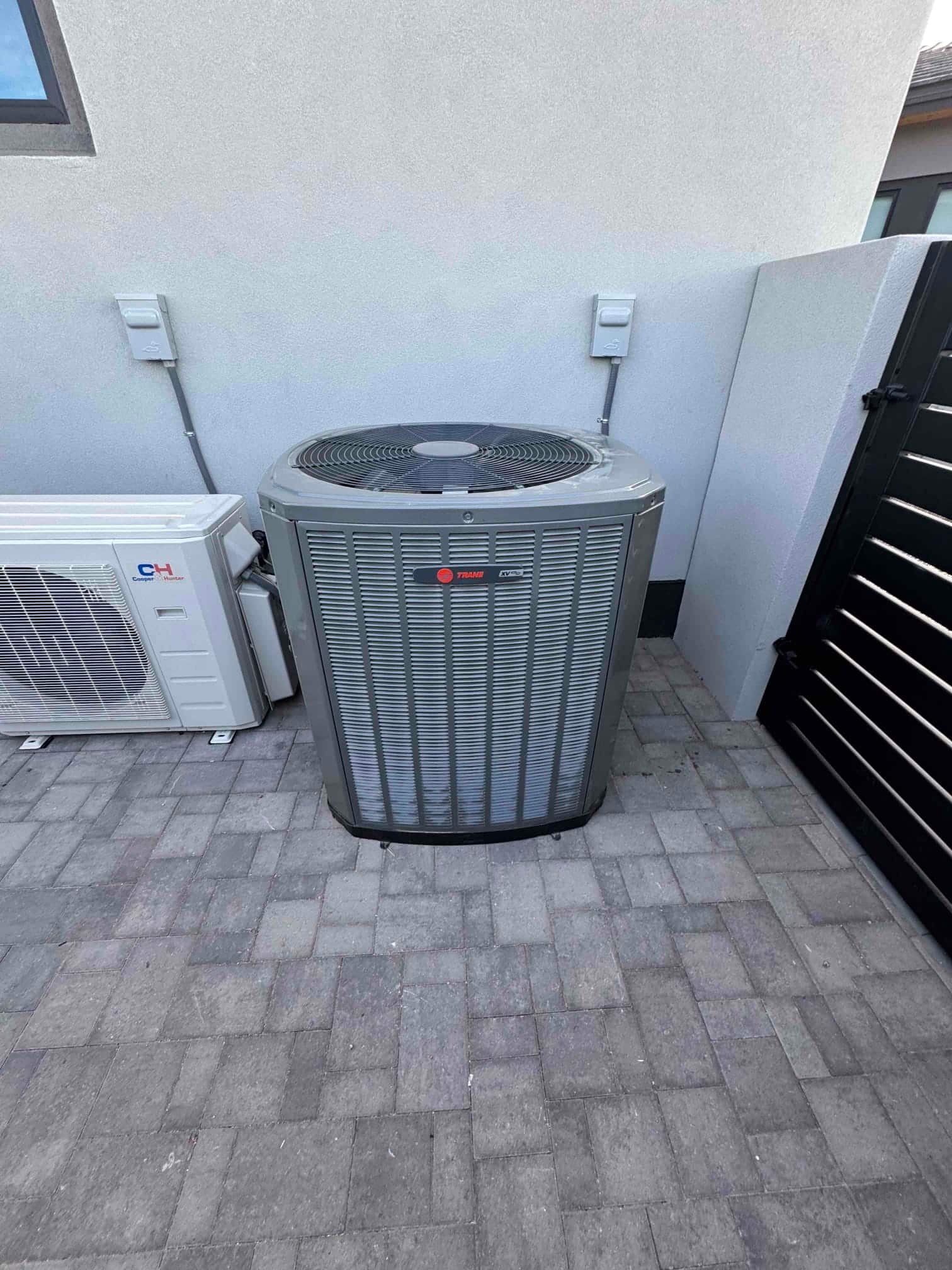 Outdoor condenser set on a paved area with nearby disconnects and adjacent mini-split unit, showing clean, finished installation.