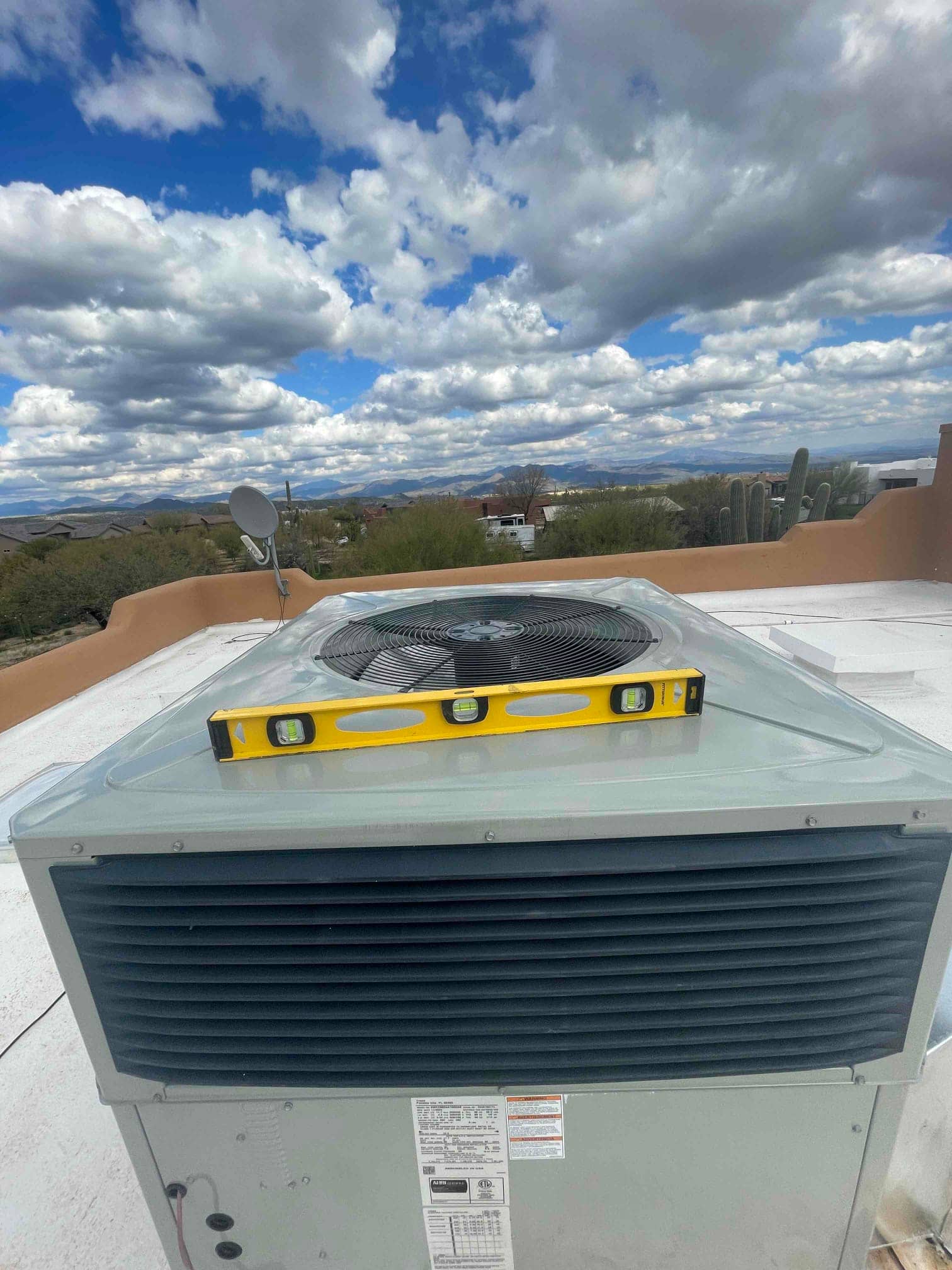 Packaged rooftop HVAC unit set in place with a level on top, showing the fan grille and intake louvers.
