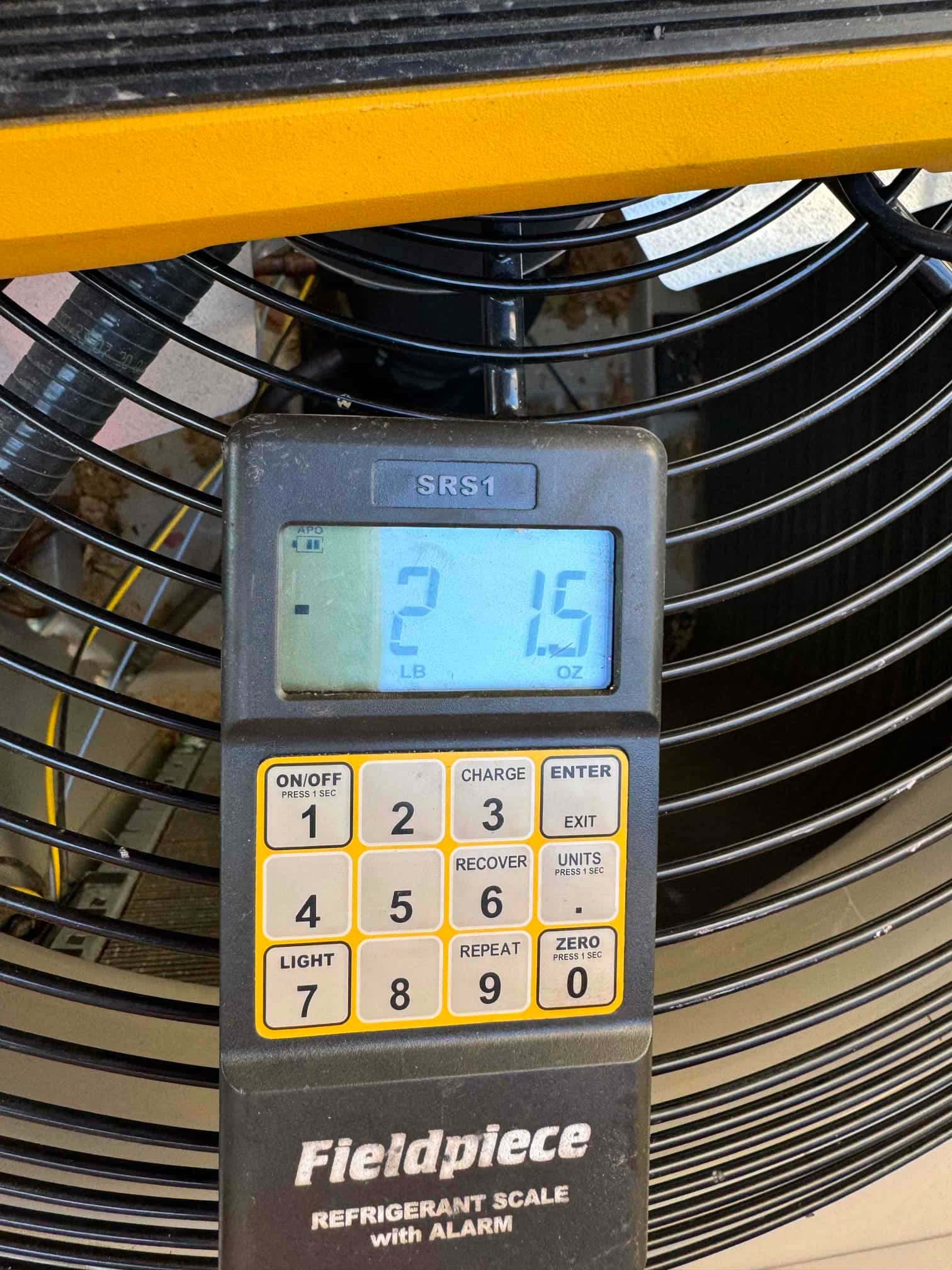 Refrigerant scale display shows 2 pounds 15 ounces during charging near the outdoor condenser fan grille.