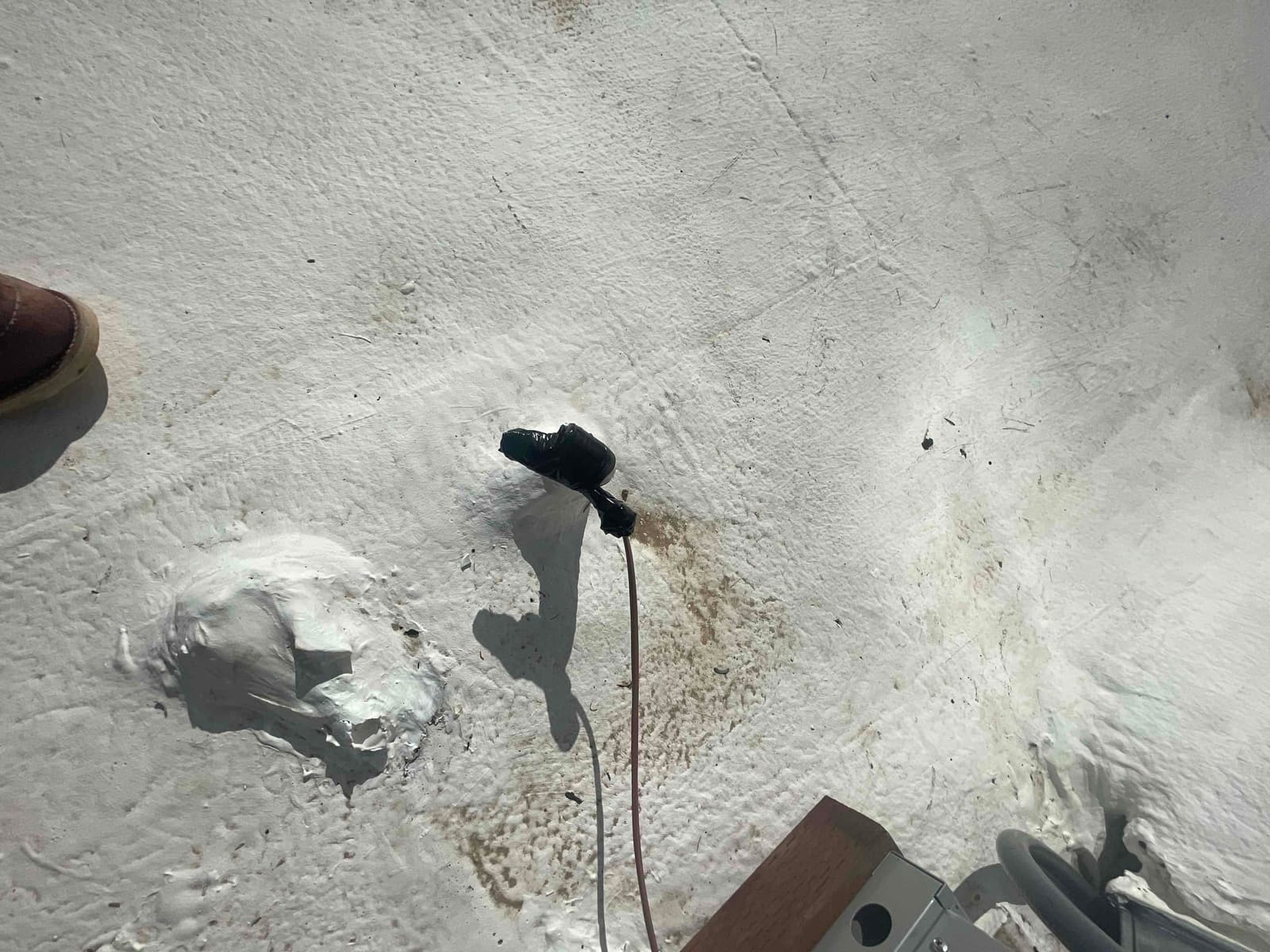 Roof penetration sealed around a low-voltage cable with mastic and tape near the condenser disconnect conduit.