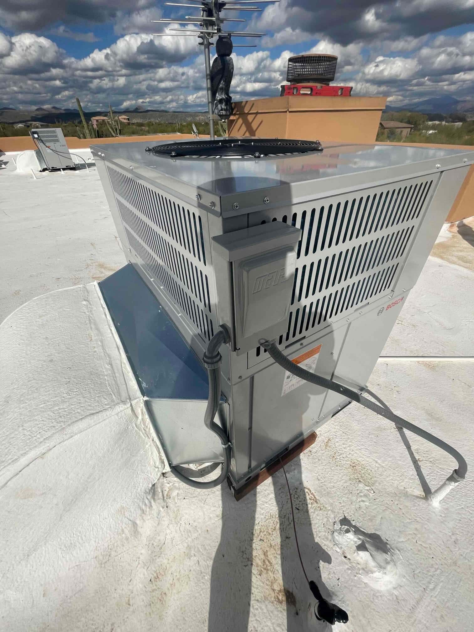 Rooftop heat pump condenser newly set on a sealed curb with flexible electrical conduit and condensate drain visible.