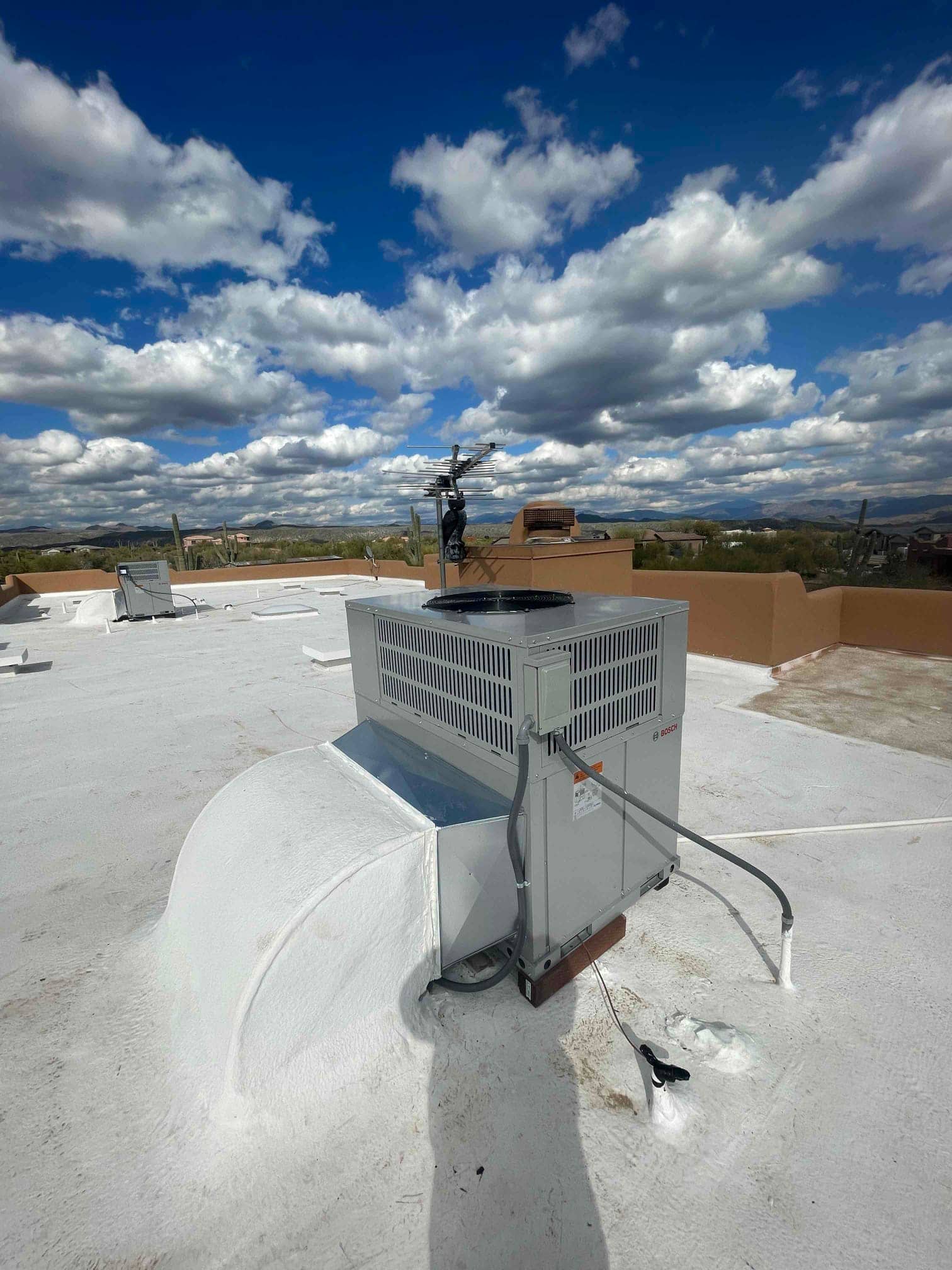 Rooftop heat pump package unit set on a coated roof with curb connection, electrical disconnect, and insulated condensate drain.