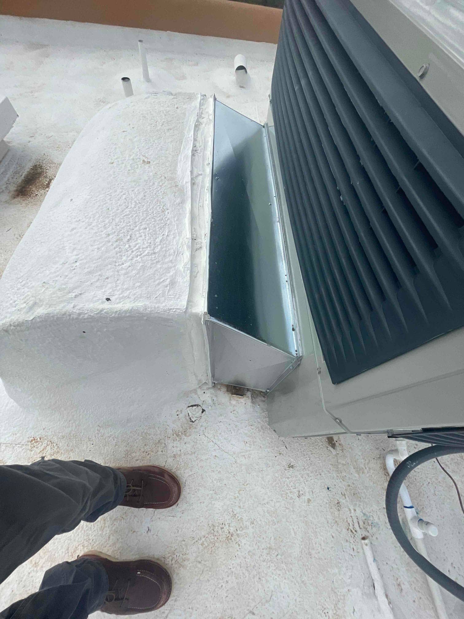 Rooftop package unit with newly fabricated sheet-metal transition curb sealed to the roof, showing duct connection and condensate piping nearby.