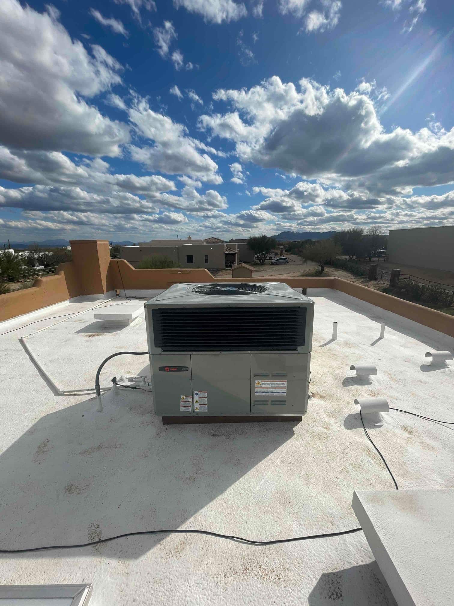 Rooftop packaged HVAC unit installed on a coated roof with electrical whip and drain piping routed to the side.