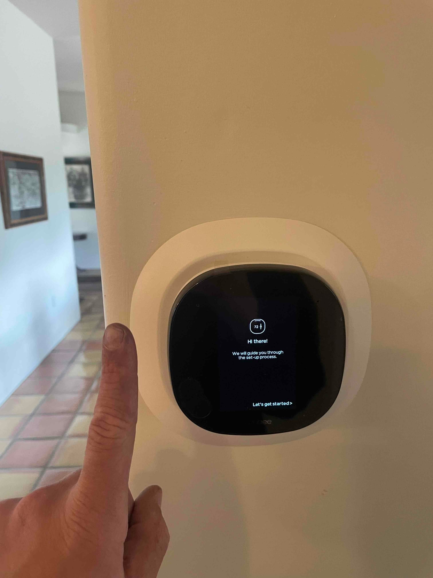 Smart thermostat on wall displays setup screen while technician points to start the configuration.