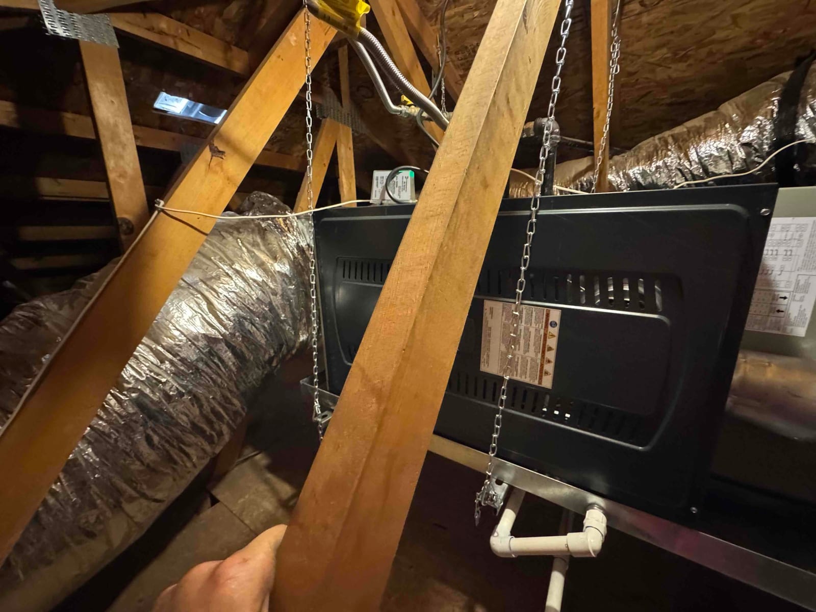Suspended air handler installed in attic with insulated flex duct connections and condensate drain piping routed to the drain pan.