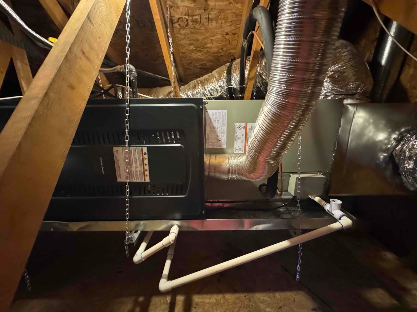 Suspended attic air handler installed with insulated duct connections and PVC condensate drain piping routed to a trap and cleanout.