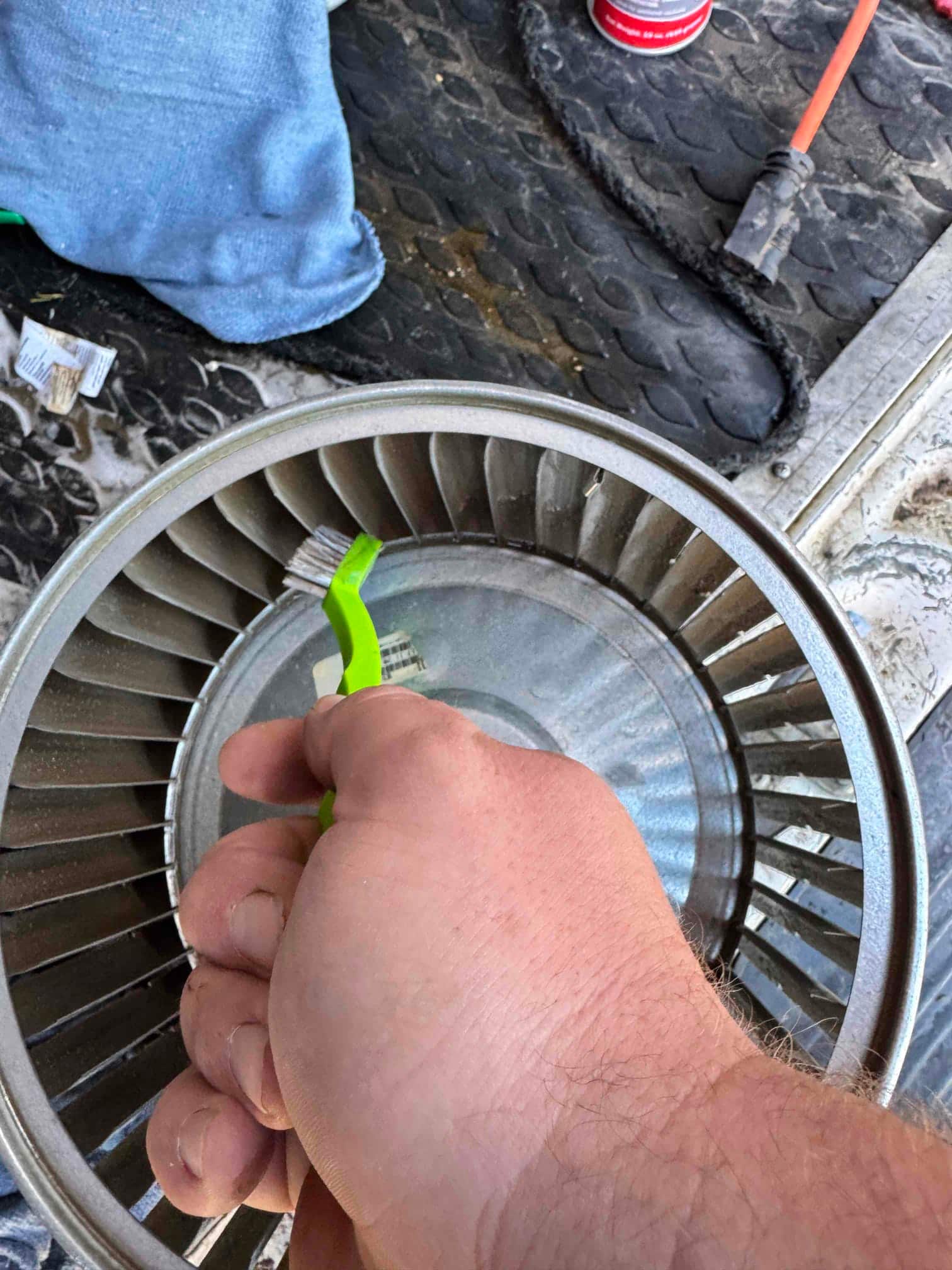 Technician hand cleans a blower wheel with a small brush before reinstallation, showing dust removal from the metal fins.