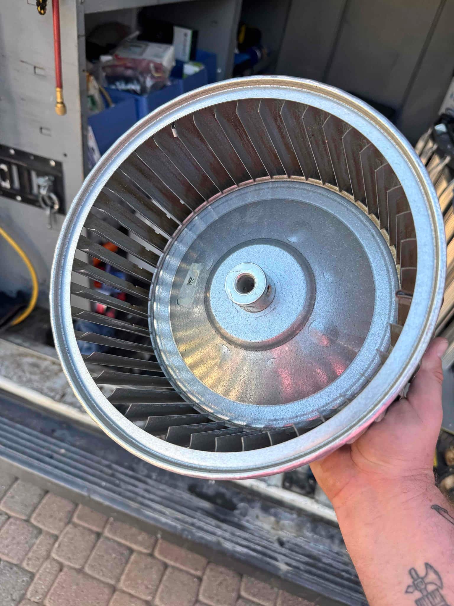 Technician holds a cleaned HVAC blower wheel assembly with visible fins and central hub, ready for reinstallation.