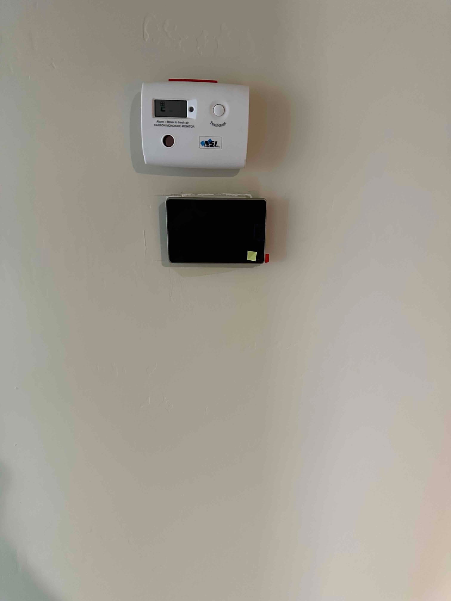 Wall-mounted carbon monoxide monitor above a newly installed thermostat with protective film, completing the control setup for the HVAC system.