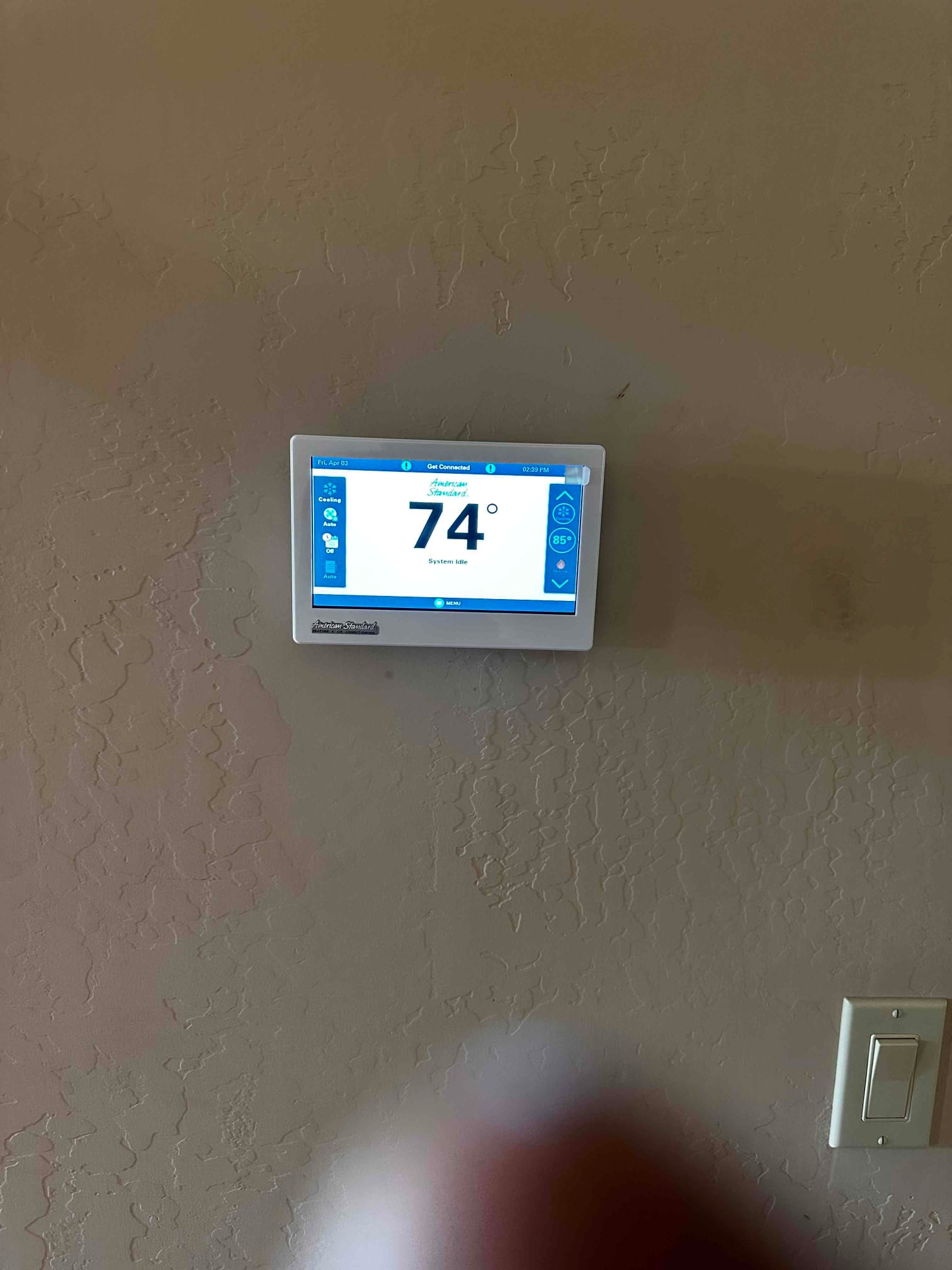 Wall-mounted digital thermostat installed and operating, displaying 74 degrees with cooling mode indicators visible.