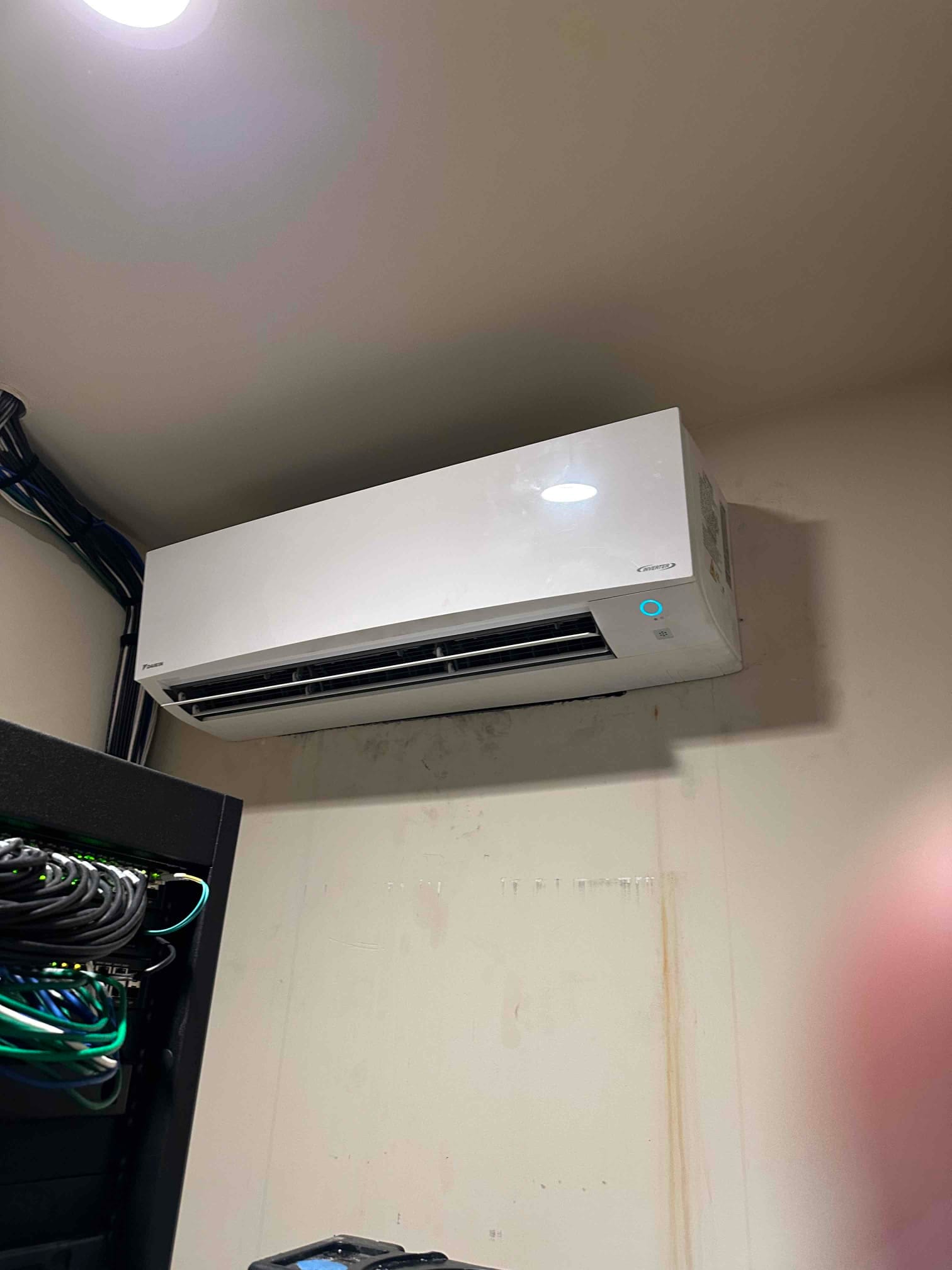 Wall-mounted mini-split indoor unit installed and operating, with louvers open and indicator light on in a finished room.