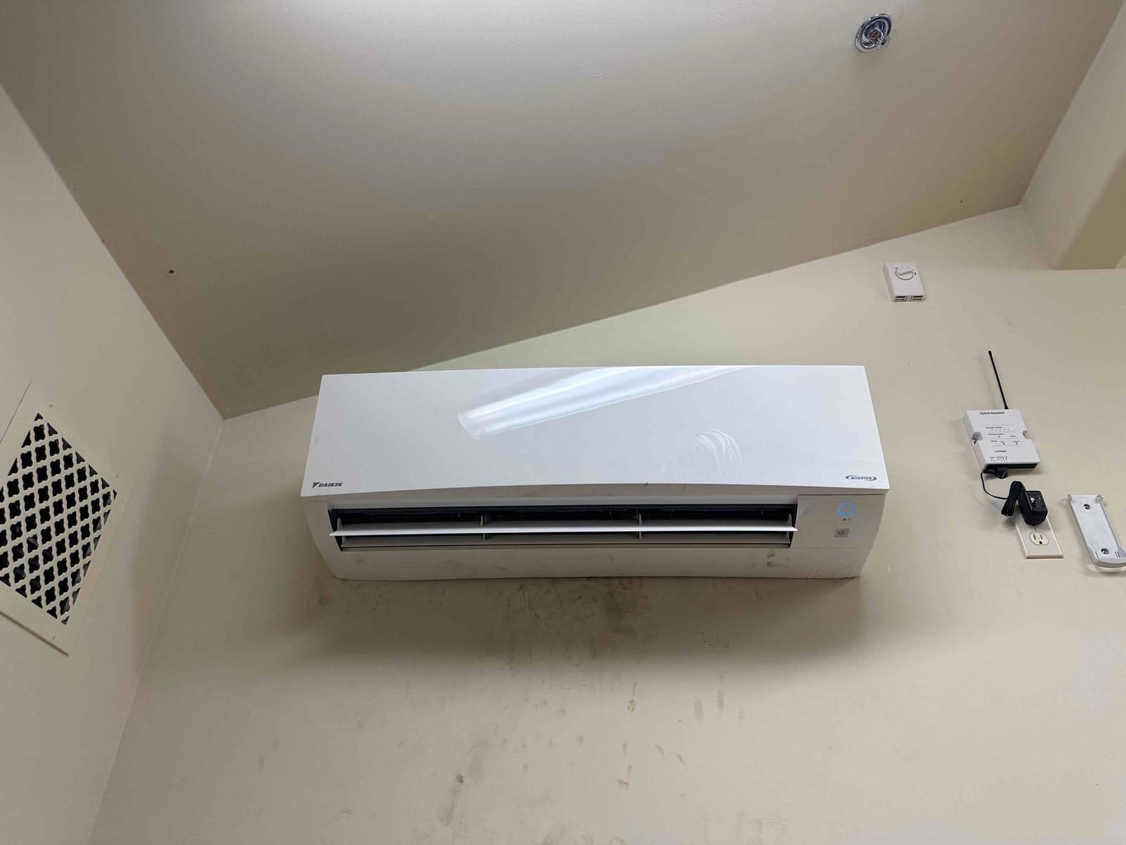 Wall-mounted mini-split indoor unit installed and powered on, with nearby control module and wall outlet visible.