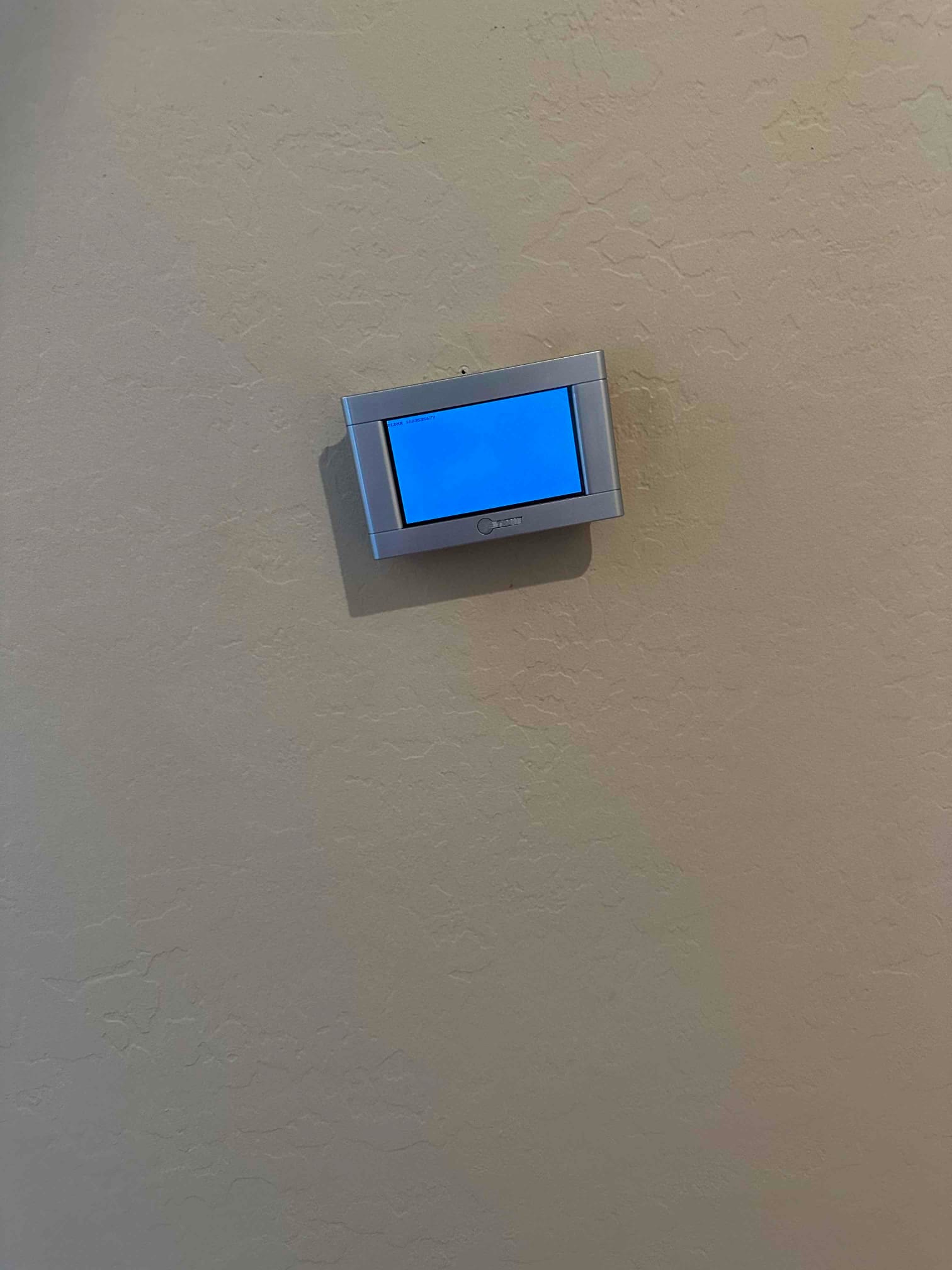 Wall-mounted thermostat with blank illuminated screen installed on finished interior wall during HVAC installation.