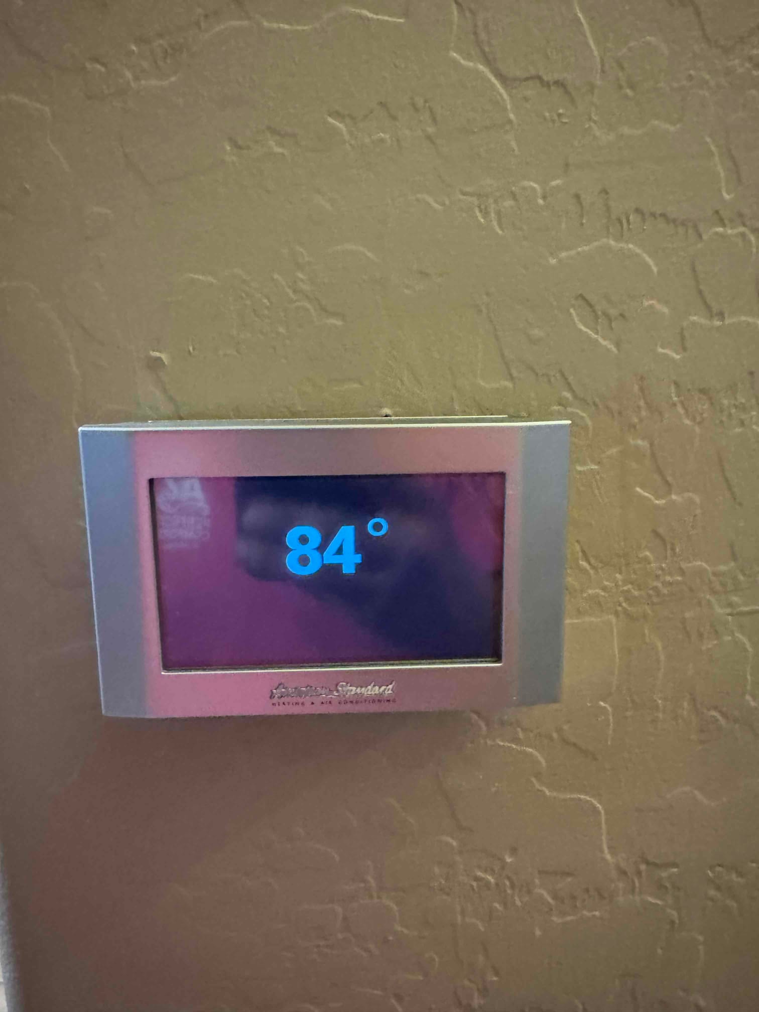 Wall-mounted thermostat display shows an indoor temperature reading of 84 degrees during system checkout.