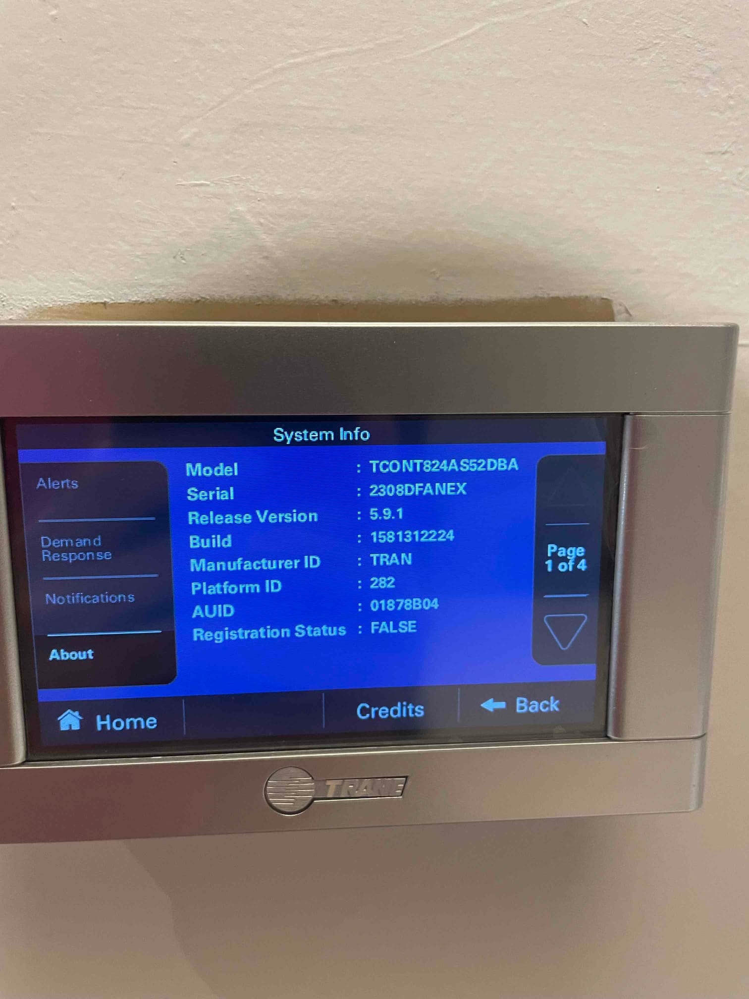Wall-mounted thermostat displaying system information screen after installation, showing model, serial, and software version details.