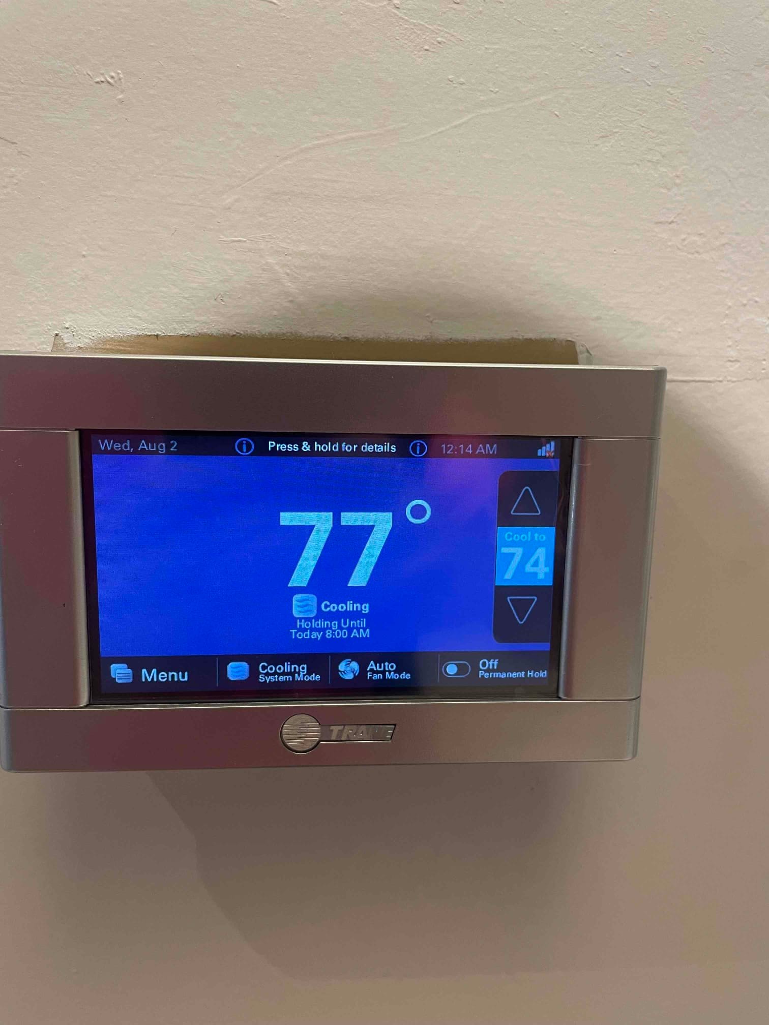 Wall-mounted touchscreen thermostat displays 77 degrees with cooling mode active and a setpoint of 74.