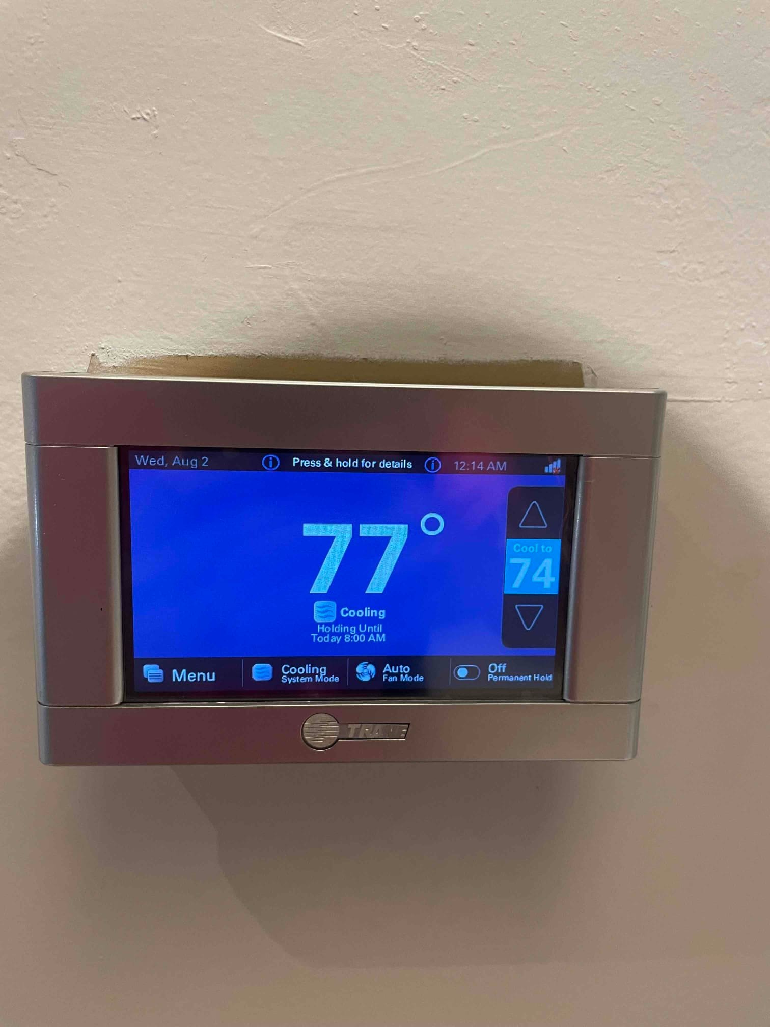Wall-mounted touchscreen thermostat displays indoor temperature at 77 degrees with cooling mode active and setpoint at 74.