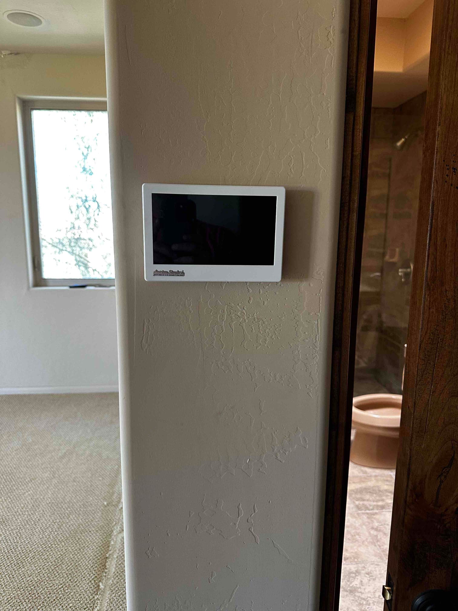 Wall-mounted touchscreen thermostat installed in a finished interior hallway, ready for system control and scheduling.