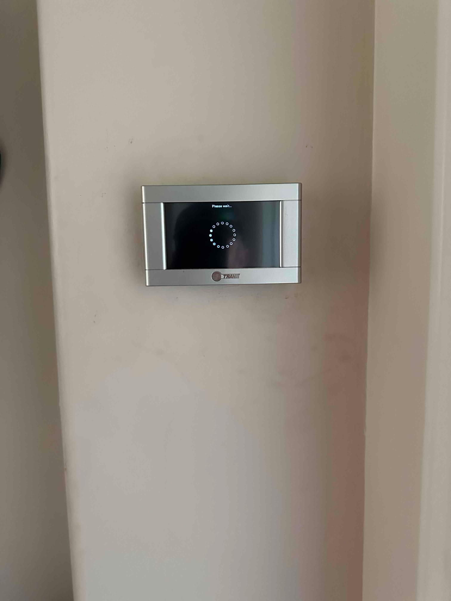 Wall-mounted touchscreen thermostat powers up with a loading message after installation, completing controls setup for the new HVAC system.