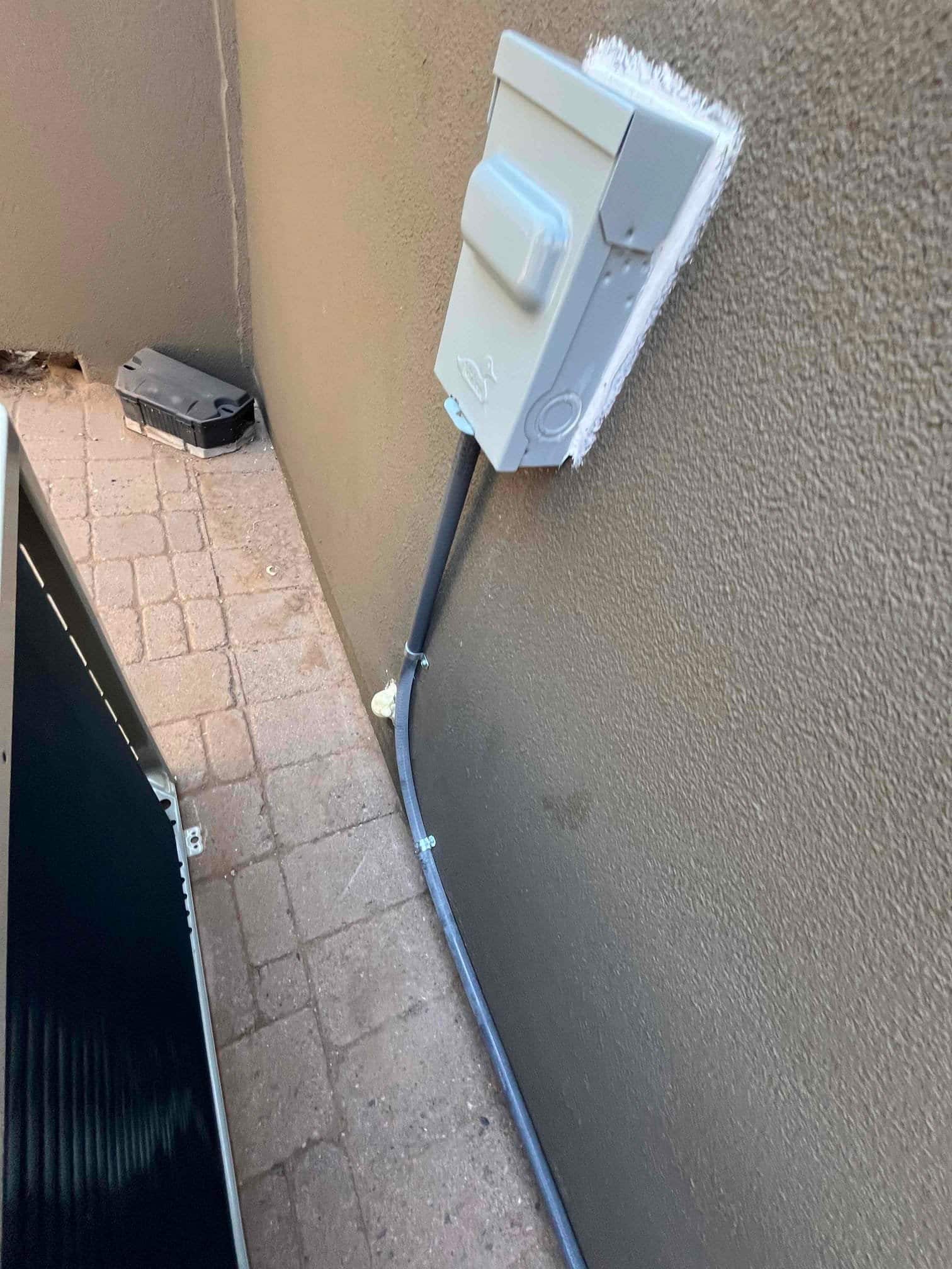 Weatherproof disconnect and sealed conduit installed on exterior wall beside the outdoor unit, with tidy routing and mounting hardware.