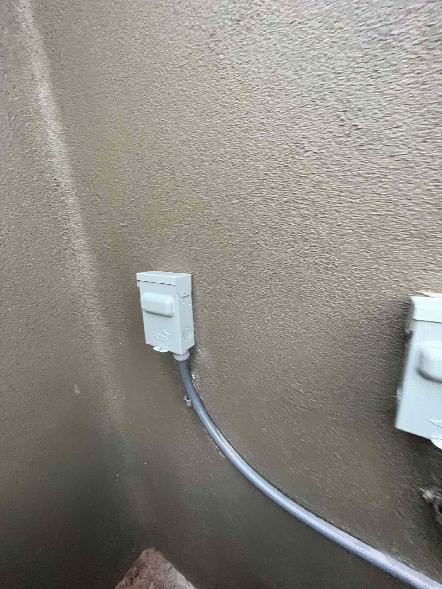Weatherproof electrical disconnect boxes mounted on exterior wall with sealed conduit routing for the new HVAC condenser.